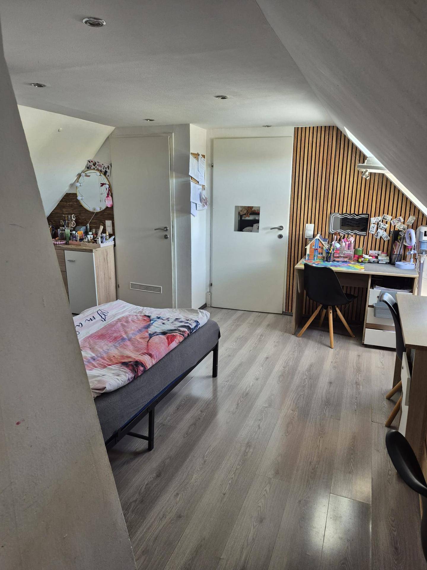 Gemütliches Schlafzimmer im Dachgeschoss mit Holzwandverkleidung und Schreibtischbereich.