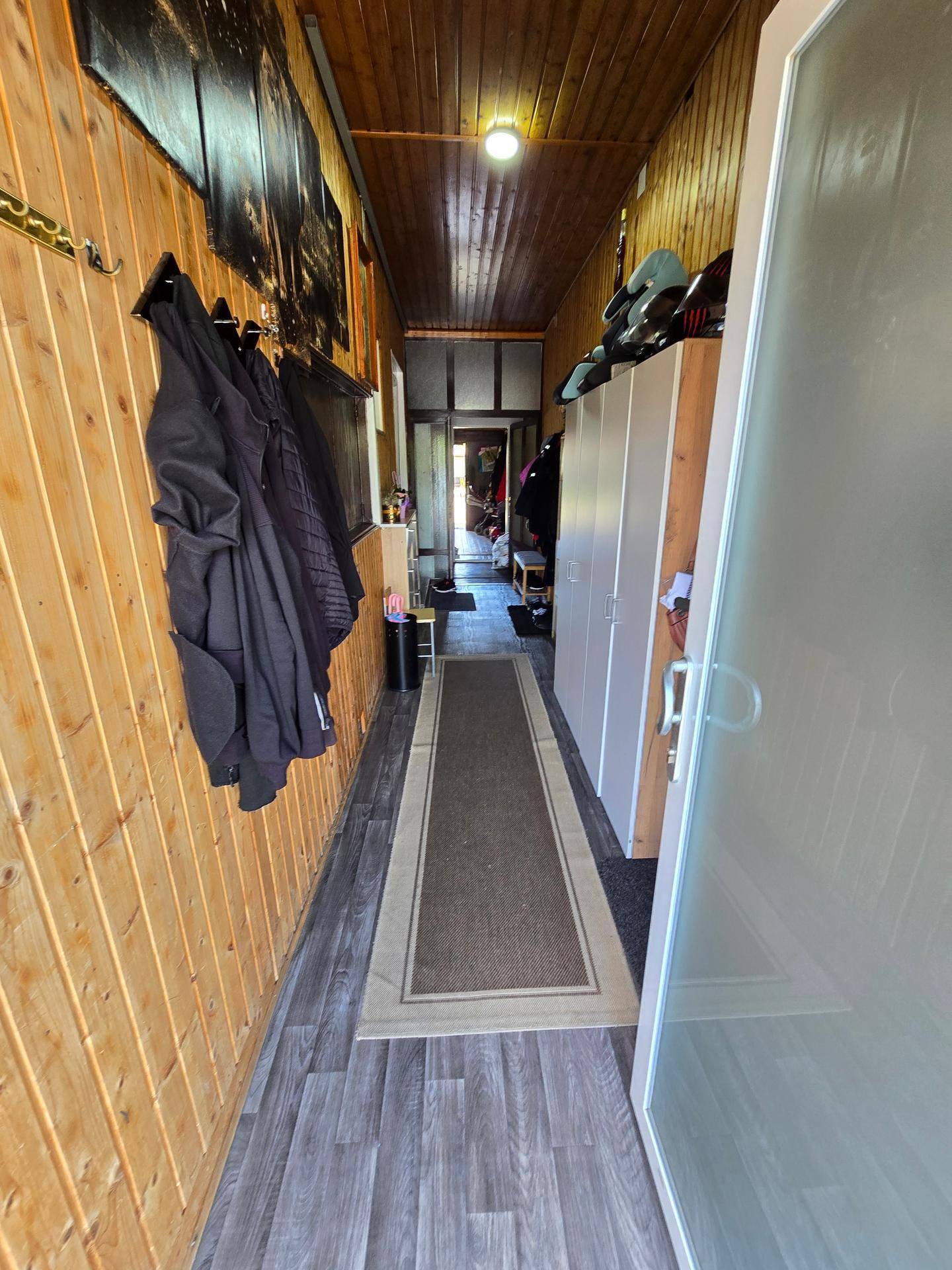 Langer, schmaler Flur mit Holzverkleidung an Wänden und Decke sowie dunklem Laminatboden.