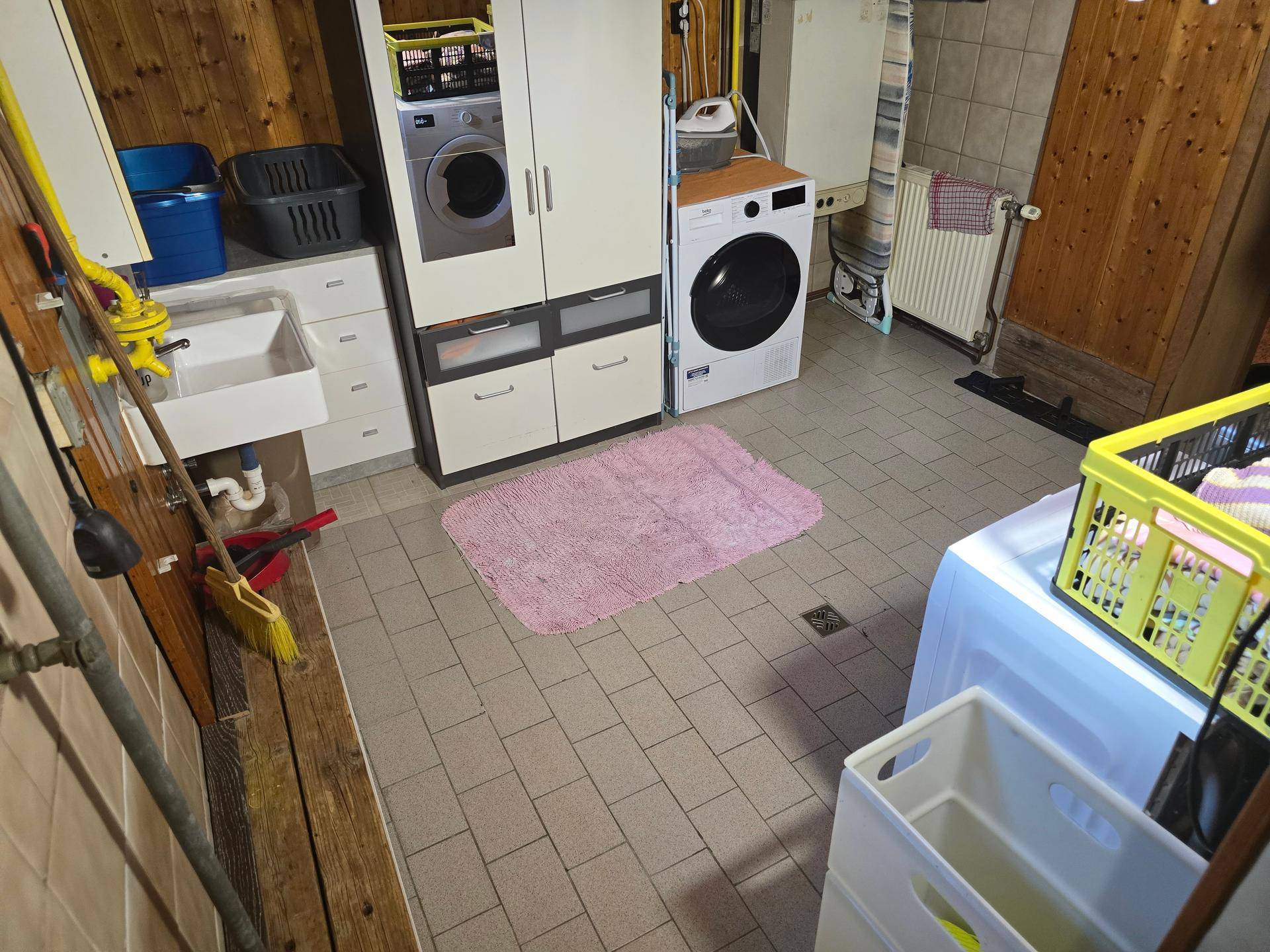 Waschküche im Keller mit Waschmaschine, Trockner und gefliestem Boden.