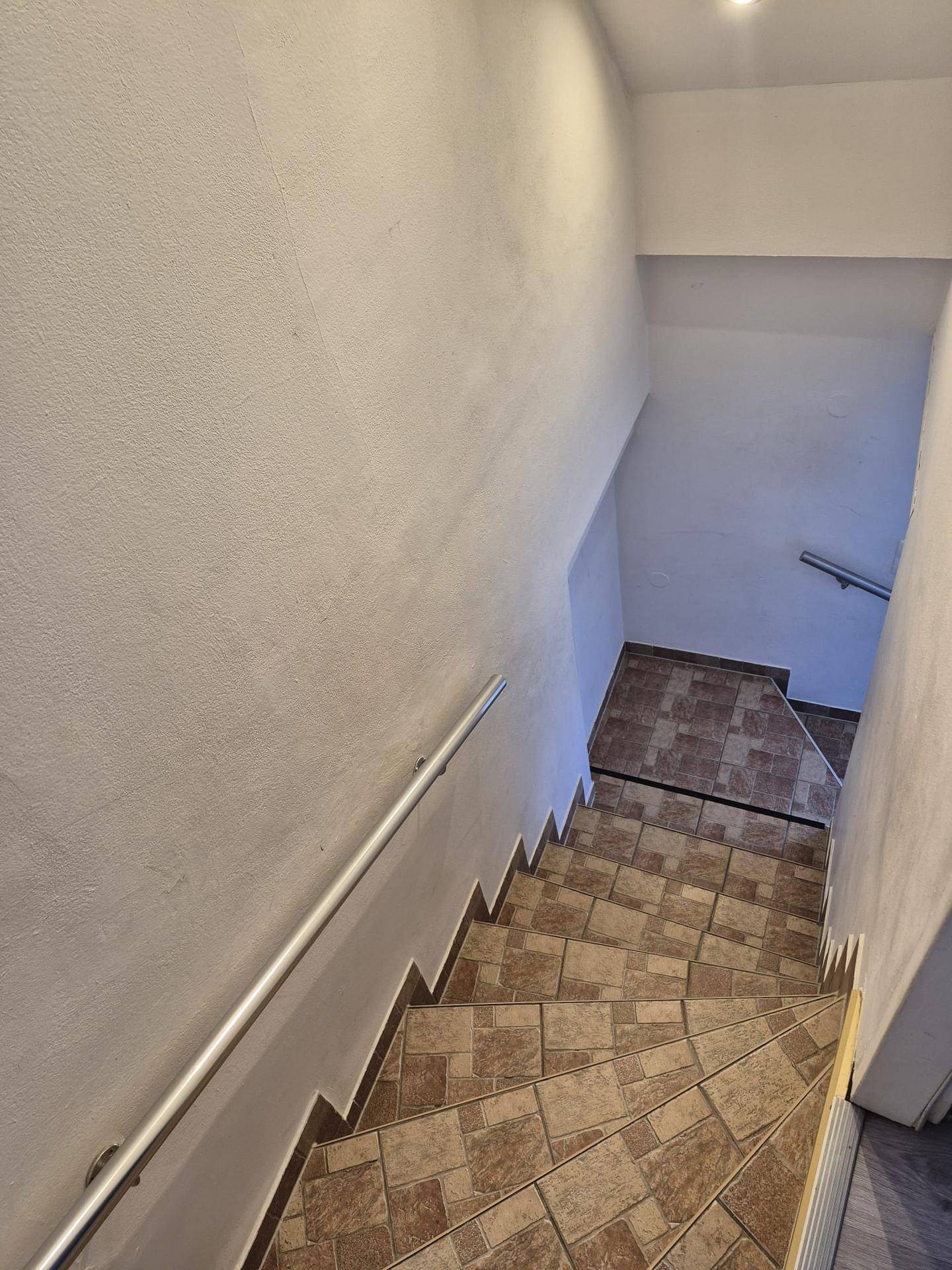 Treppenhaus mit gefliesten Stufen und einem Handlauf, der in den unteren Bereich führt.