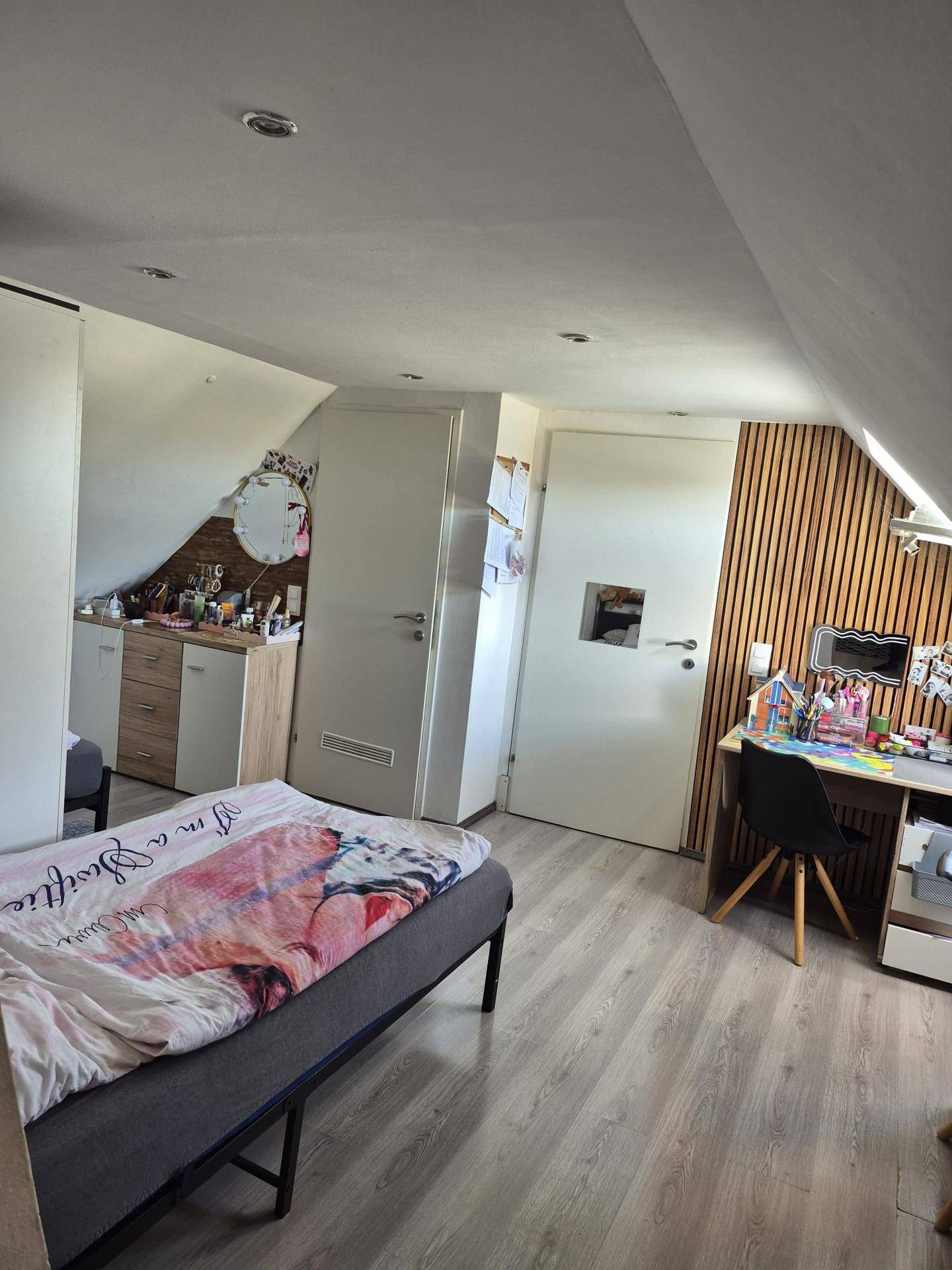 Gemütliches Schlafzimmer im Dachgeschoss mit Holzwandverkleidung und Schreibtischbereich.