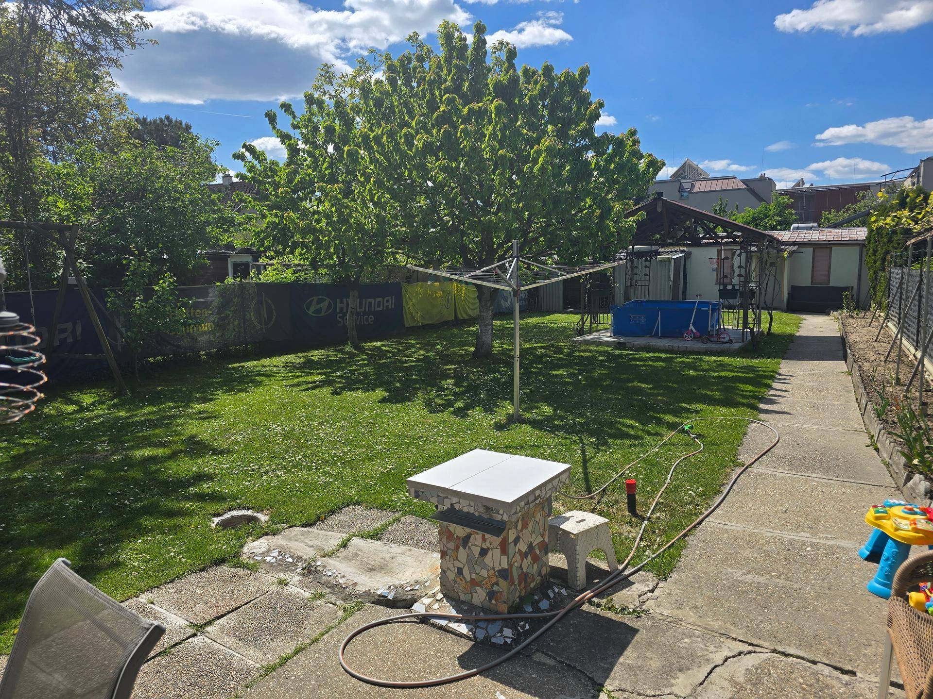 Großer Garten mit Rasen, Wäschespinne und gepflastertem Weg unter blauem Himmel.