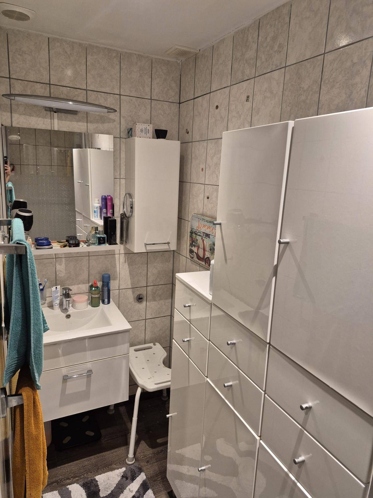 Badezimmer mit weißem Waschbecken, Spiegelschrank und glänzenden weißen Schränken.