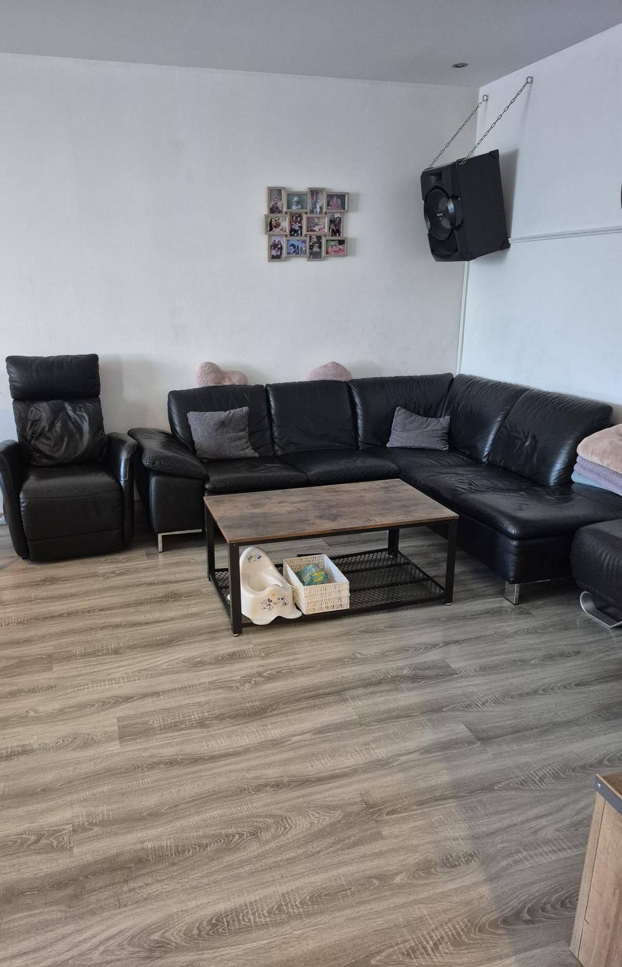 Geräumiges Wohnzimmer mit schwarzem Ledersofa, Couchtisch und Laminatboden.