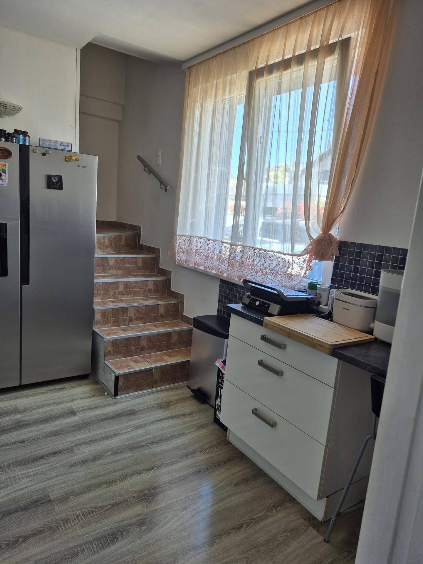 Küche mit Kühlschrank, Arbeitsplatte und Treppe, die in einen anderen Bereich führt.
