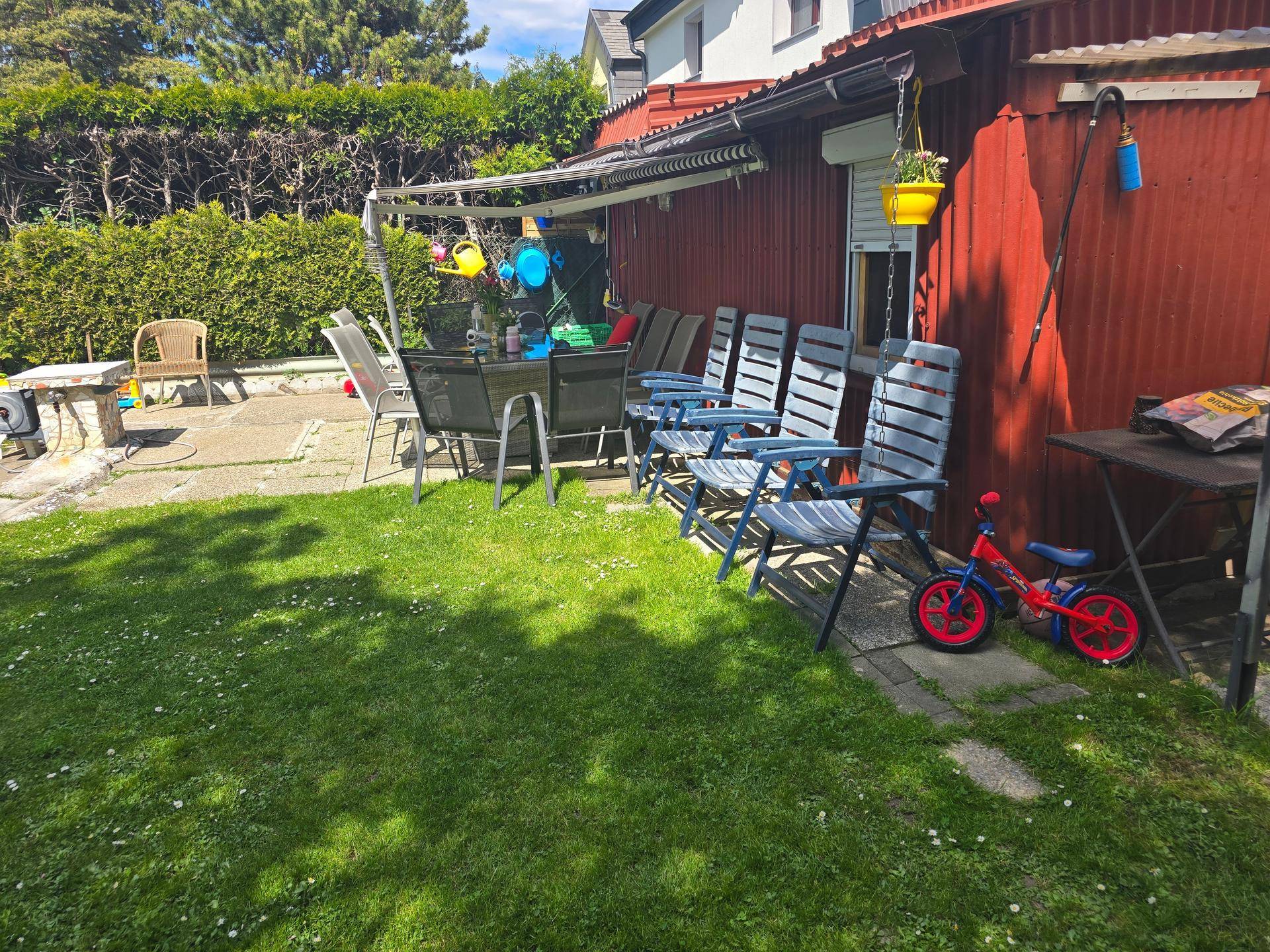 Terrasse mit Gartenmöbeln, Markise und Blick auf den grünen Garten.