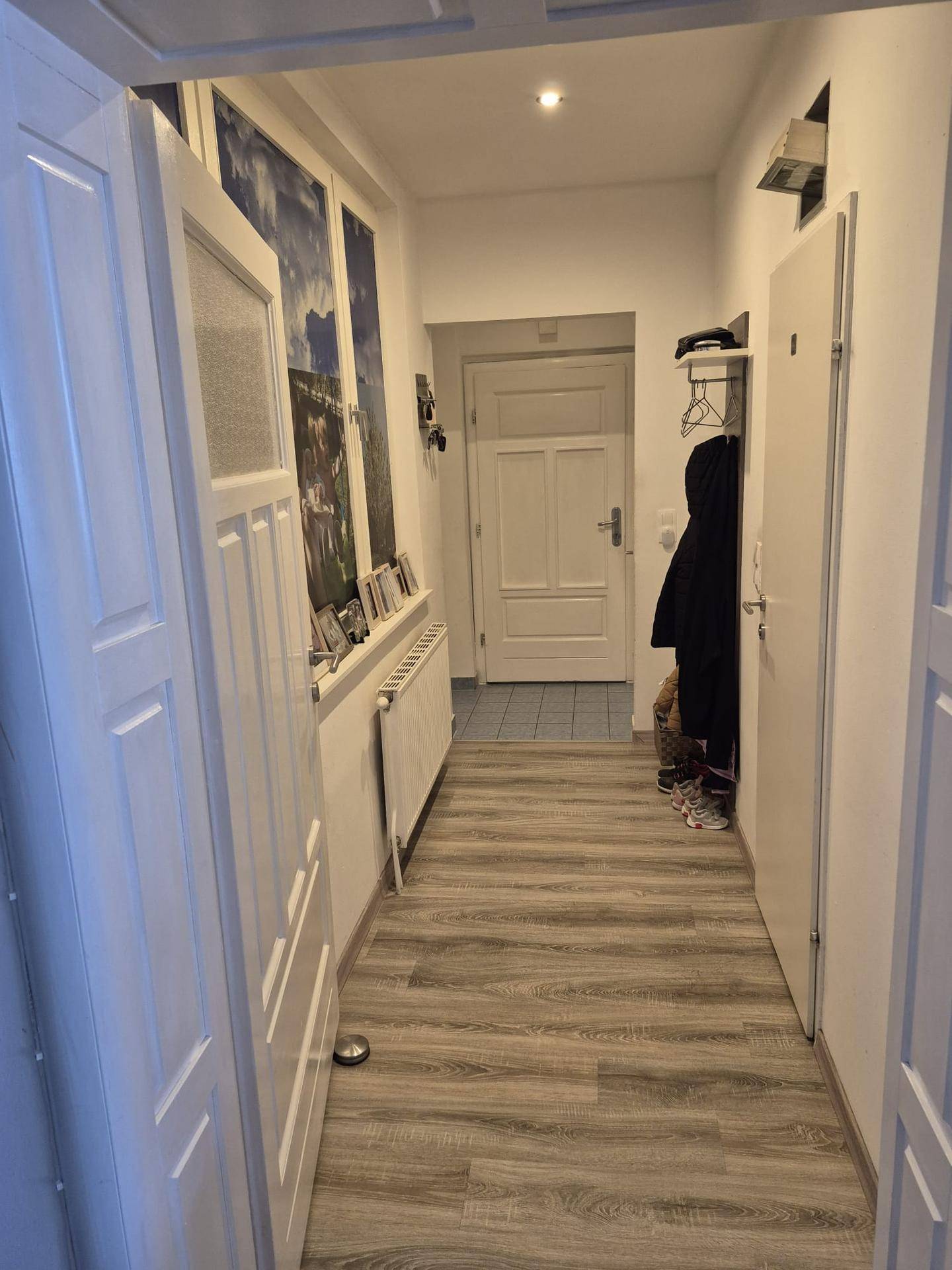 Heller Flur mit modernem Laminatboden, weißen Wänden und Heizkörper unter Bildern.