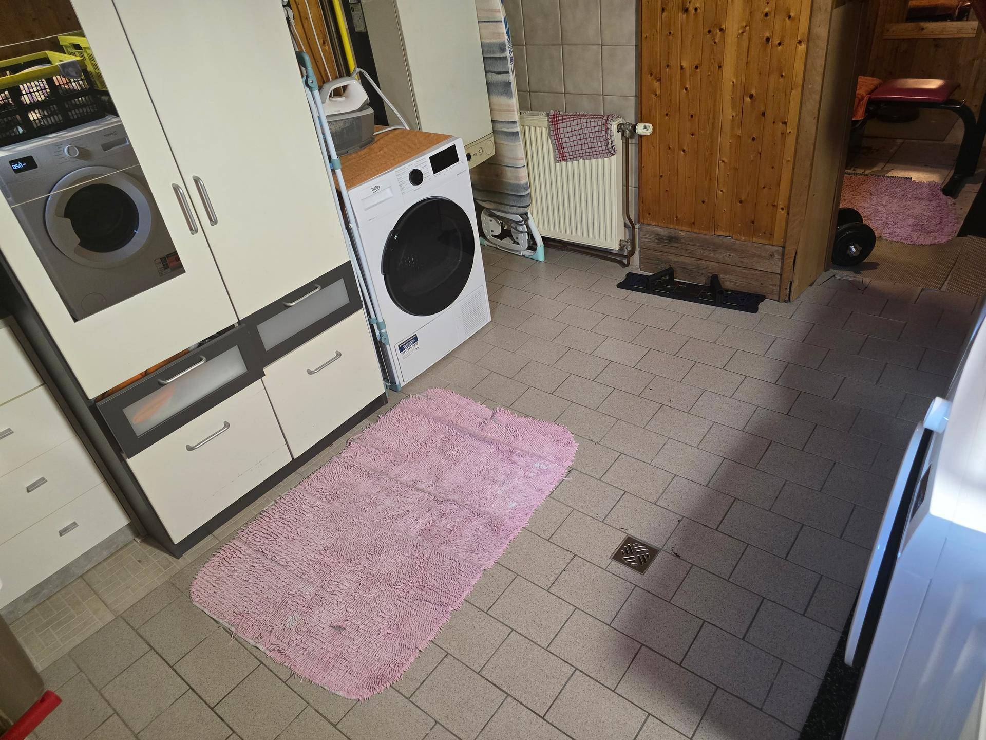 Kellerraum mit Waschmaschine, Trockner und gefliestem Boden, teilweise holzvertäfelt.
