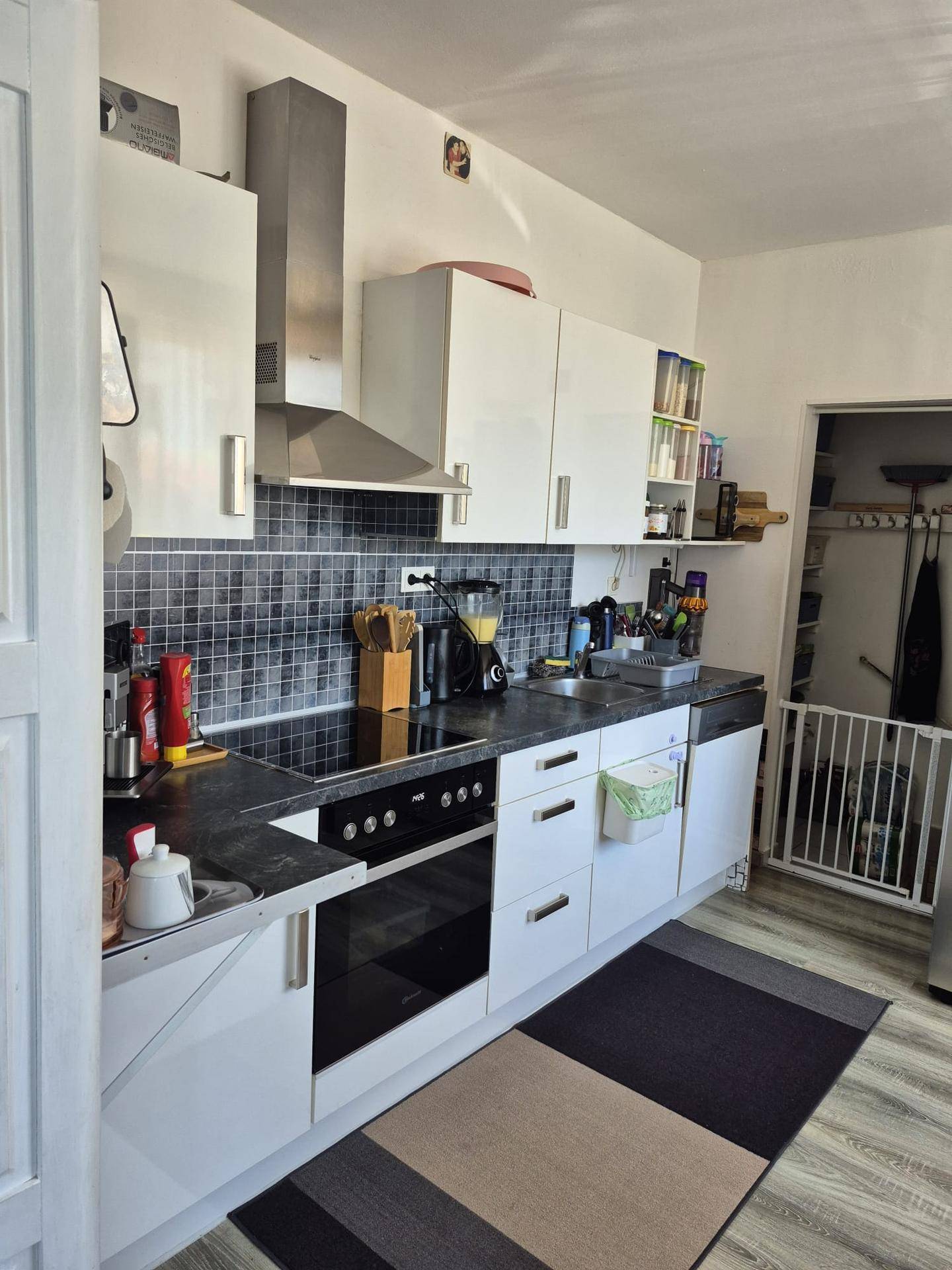 Moderne Küche mit weißen Hochglanzschränken, dunkler Arbeitsplatte und integrierten Geräten.
