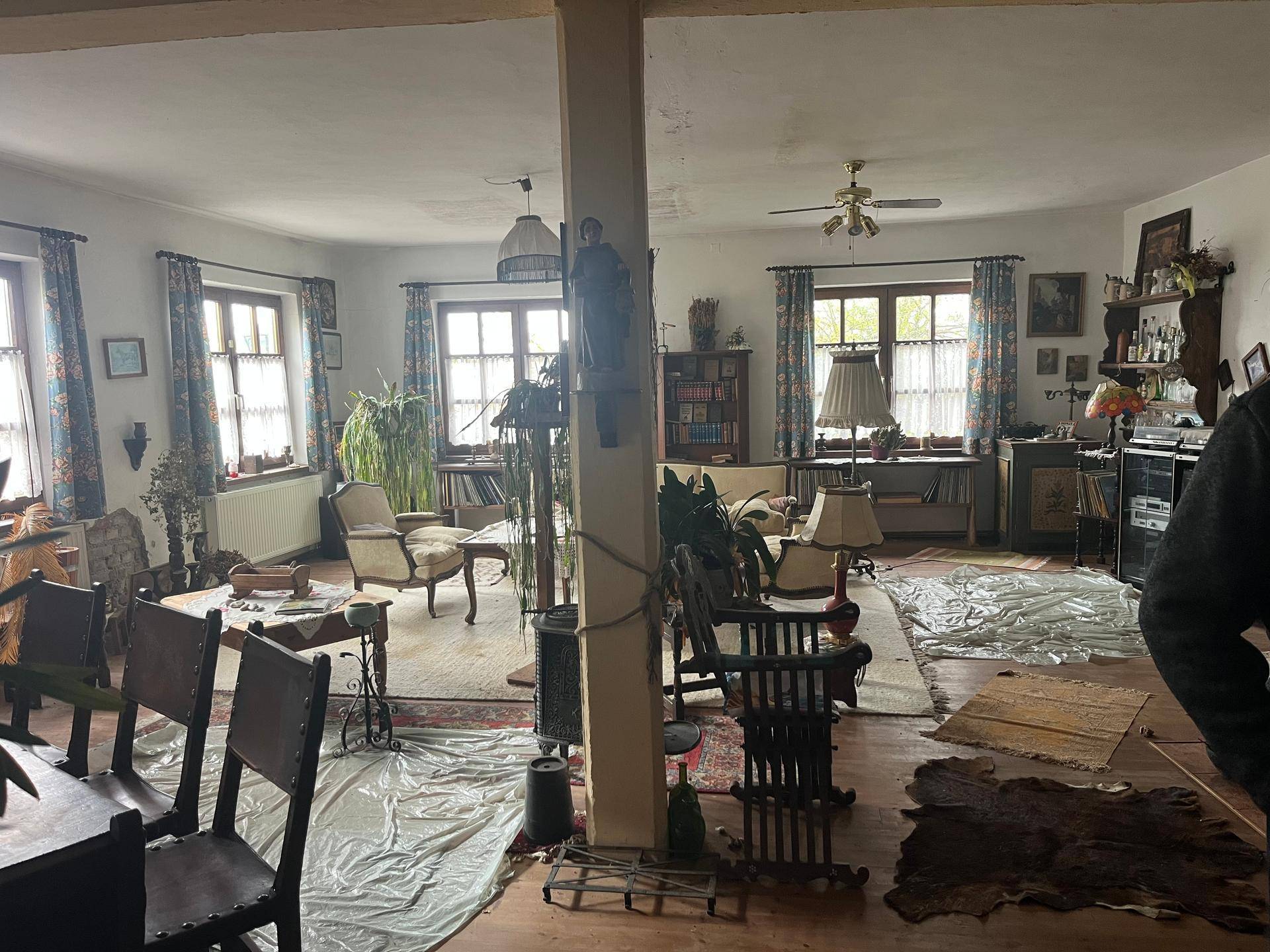 Großer Wohnbereich mit mehreren Fenstern, Holzboden und verschiedenen Sitzgelegenheiten, lichtdurchflutet und geräumig.