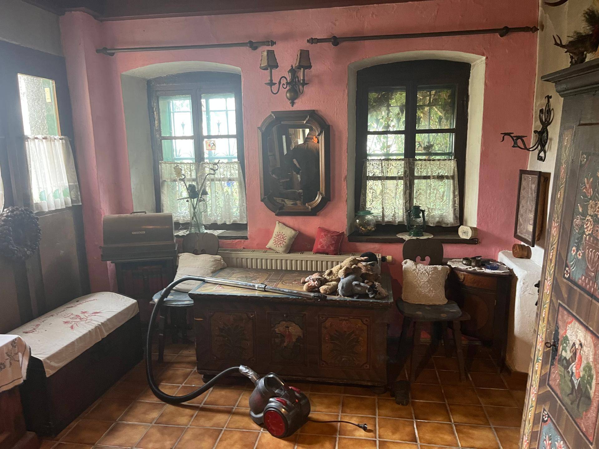 Gemütlicher Raum mit rosa Wänden, Fliesenboden und traditionellen Holzmöbeln, farbenfroh und charmant.