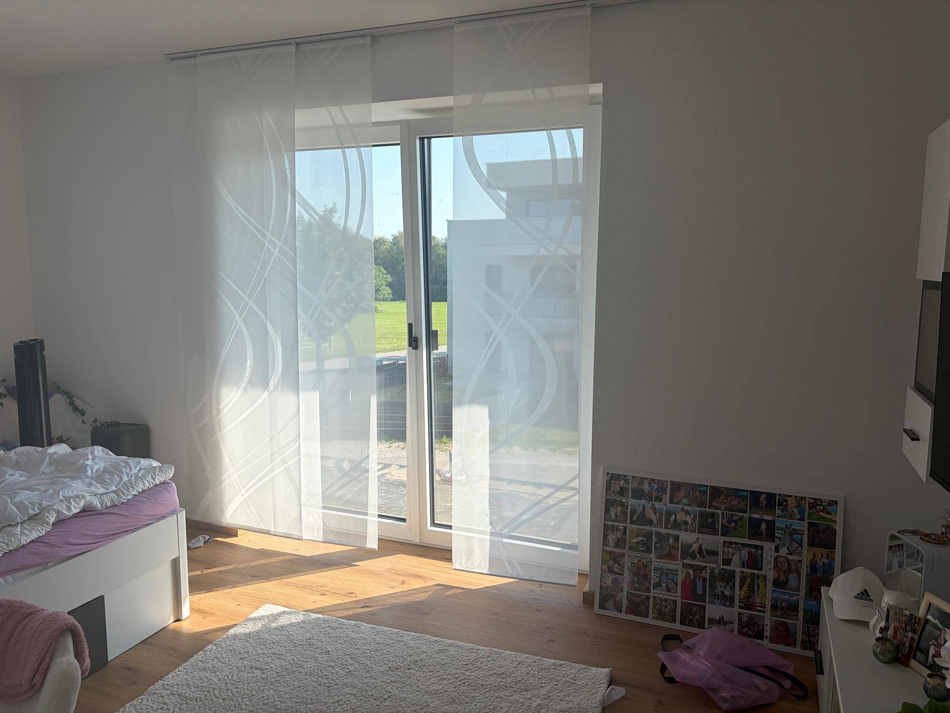 Schlafzimmer mit Holzboden, großen Fenstern und Zugang zu einem Balkon oder Garten.