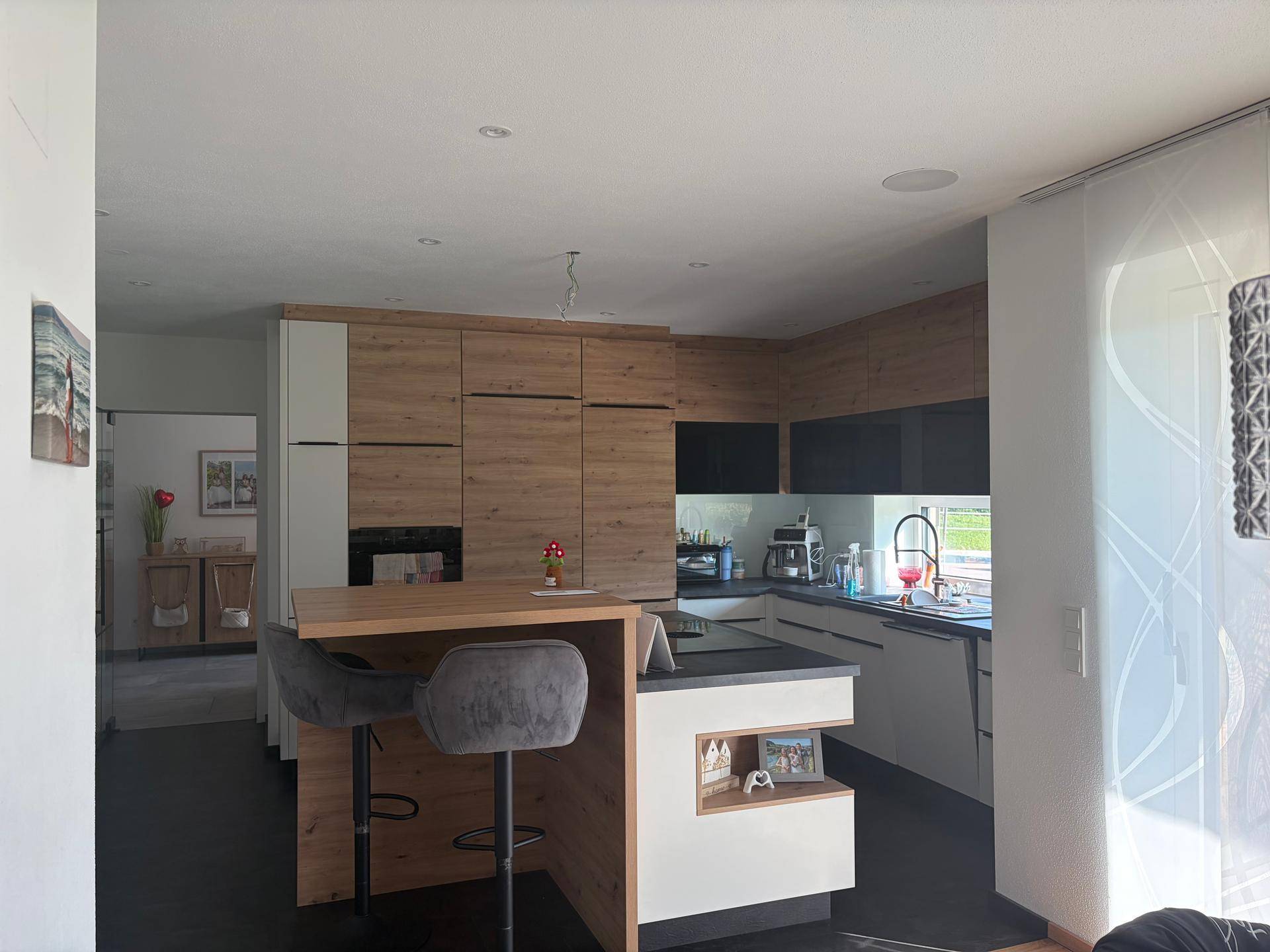 Moderne Küche mit Holzfronten, dunkler Arbeitsplatte und integrierter Frühstücksbar.