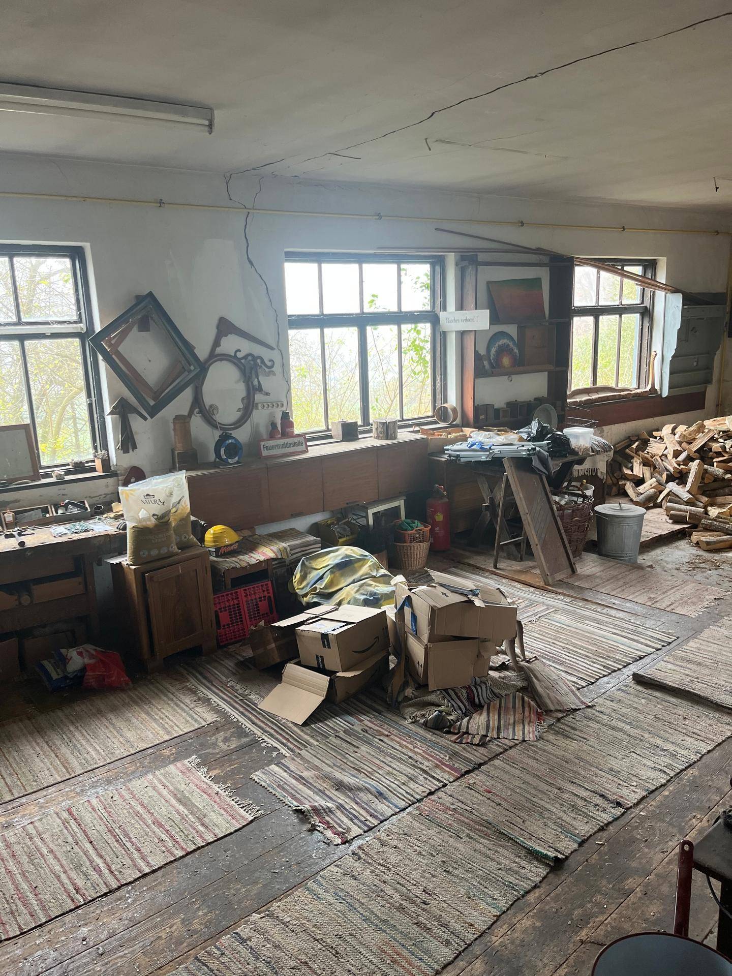 Geräumiger Werkstattraum mit großen Fenstern, Holzboden und viel Stauraum, hell und funktional.