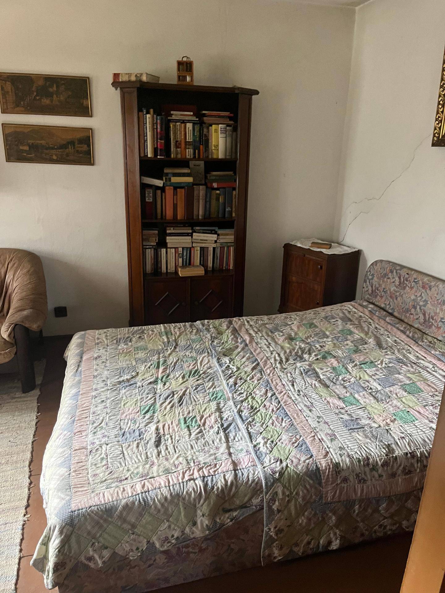 Schlafzimmer mit Doppelbett, Bücherregal und einfacher Einrichtung, ausgestattet mit Holzboden.