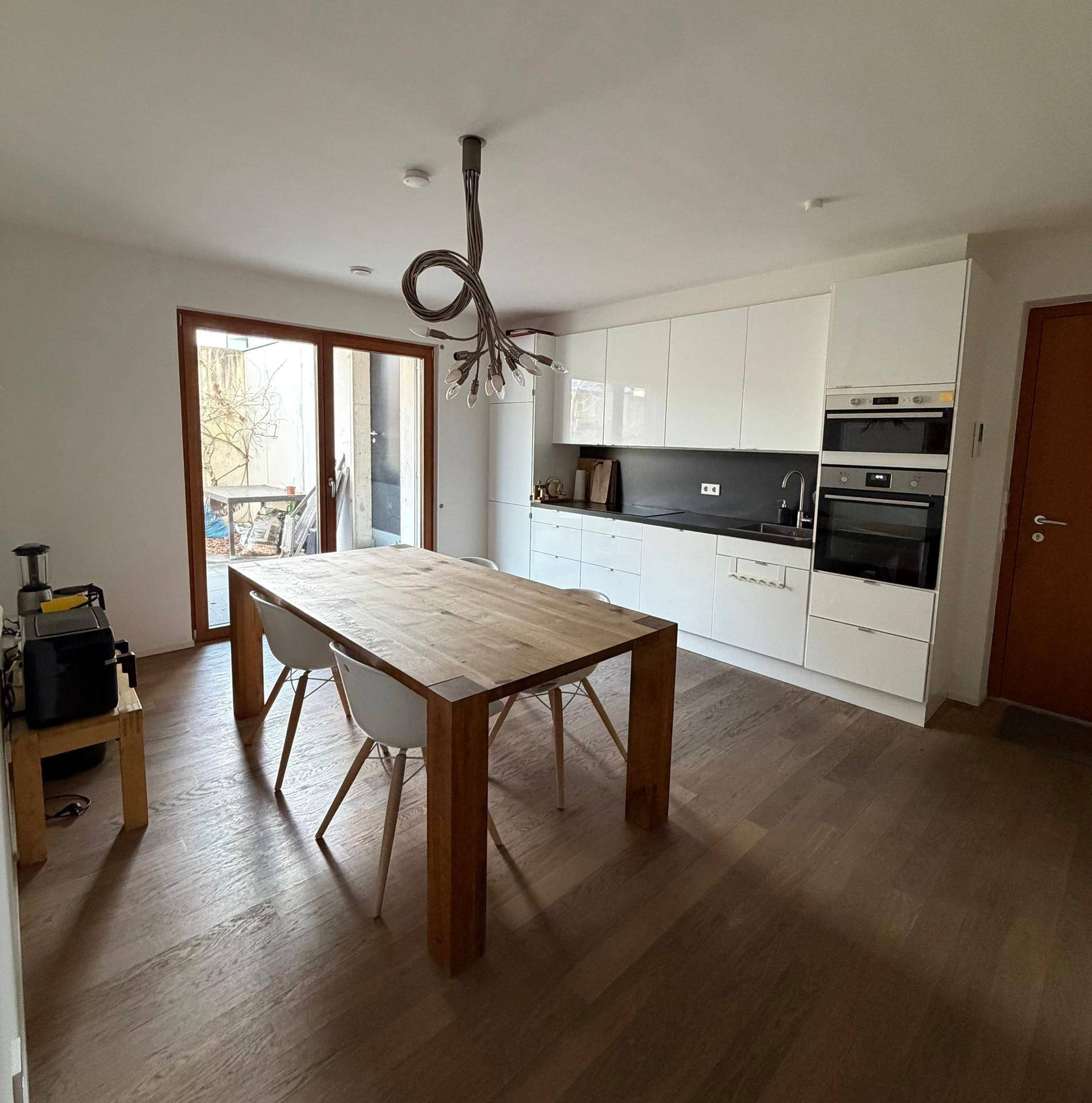 Moderne offene Küche mit weißen Hochglanzfronten, Holztisch und Terrassenzugang.