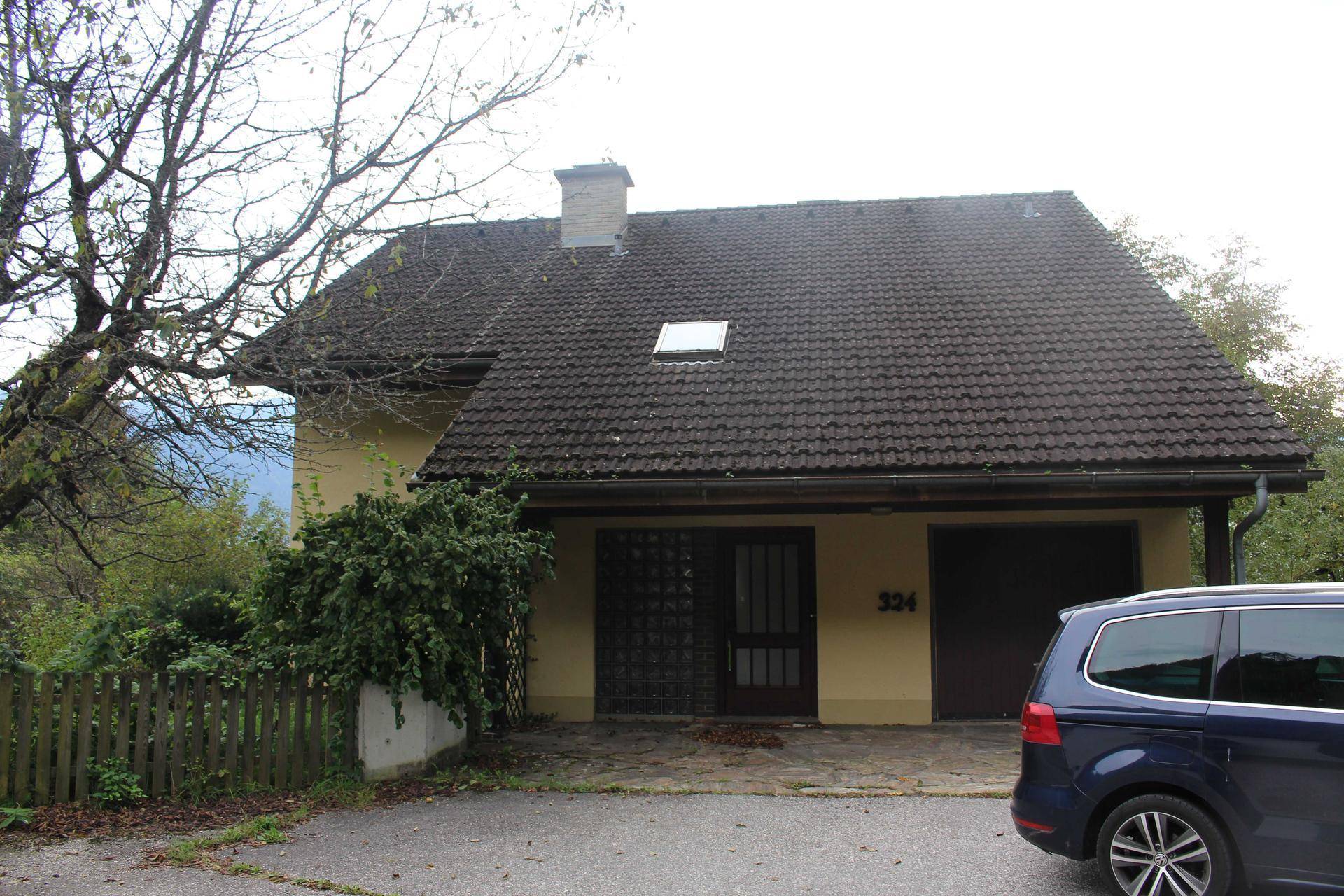Vorderansicht eines Einfamilienhauses mit Garagentor, Einfahrt und geparktem Auto.