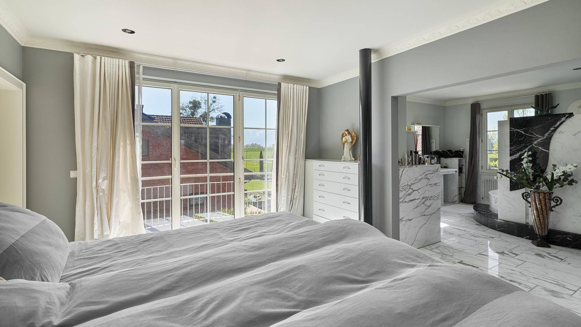 Helles Schlafzimmer mit Zugang zum Badezimmer und großen Fenstern mit Ausblick.