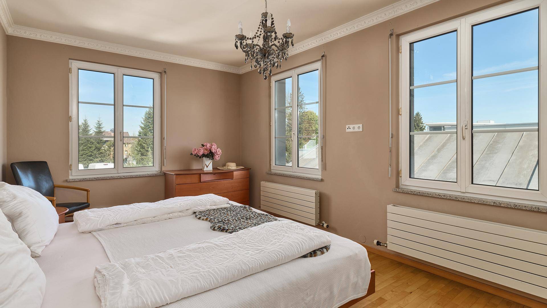 Helles Schlafzimmer mit Parkettboden, Kronleuchter und mehreren Fenstern.
