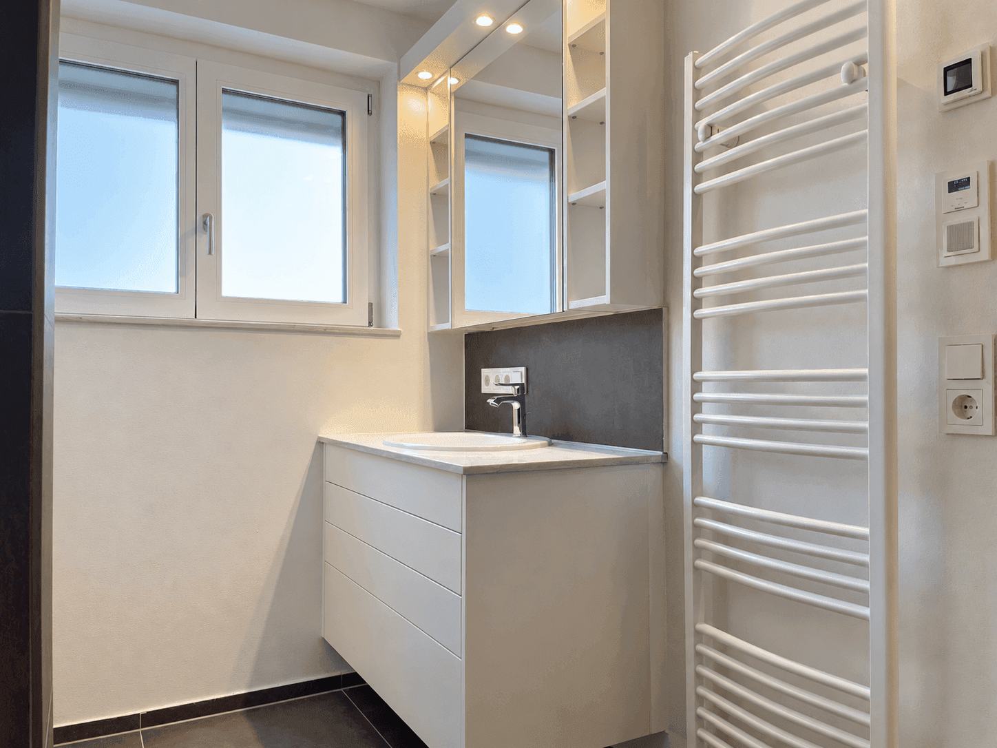 Modernes Badezimmer mit Waschtisch, Spiegelschrank, beheiztem Handtuchhalter und Fenster.