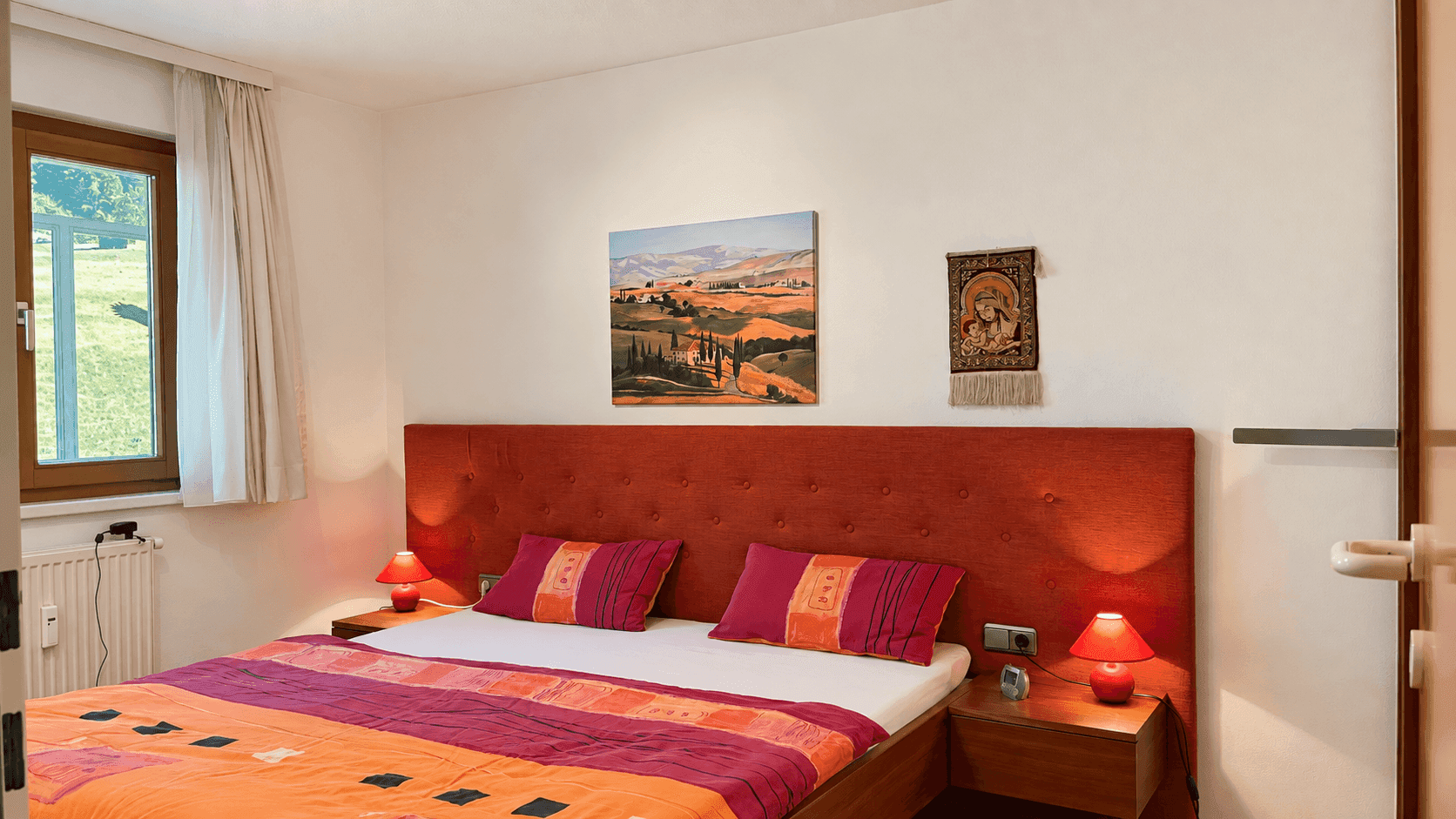Schlafzimmer mit großem Doppelbett, farbenfroher Bettwäsche und Blick ins Grüne.