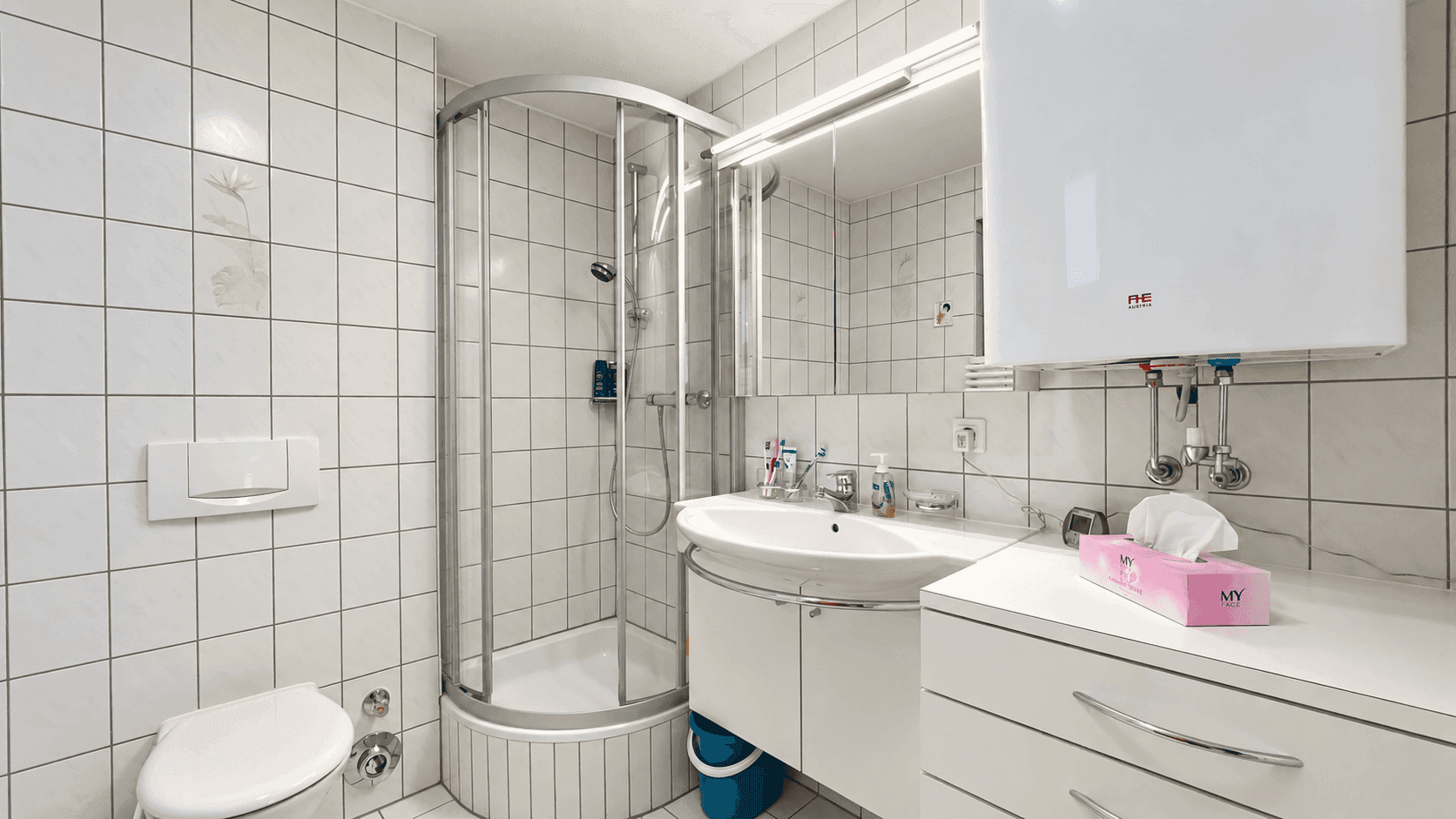 Helles Badezimmer mit Duschkabine, WC und Waschbecken mit Spiegelschrank.