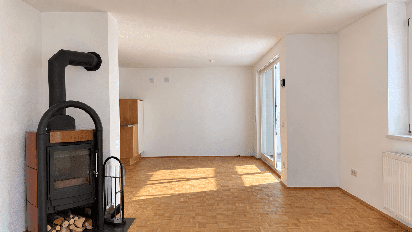 Geräumiges Wohnzimmer mit Holzboden, einem gemütlichen Holzofen und viel natürlichem Licht.