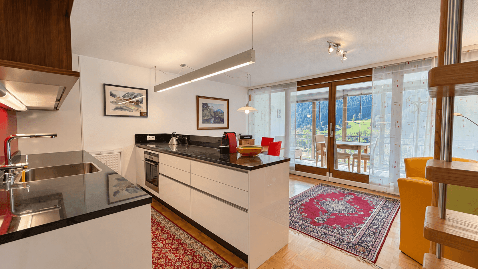 Moderne Küche mit dunkler Arbeitsplatte und Blick auf die Berge durch große Fenster.