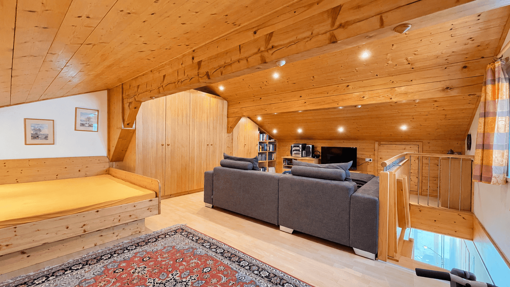 Geräumiger Dachboden mit Holztäfelung, Sofa und Stauraum unter der Dachschräge.