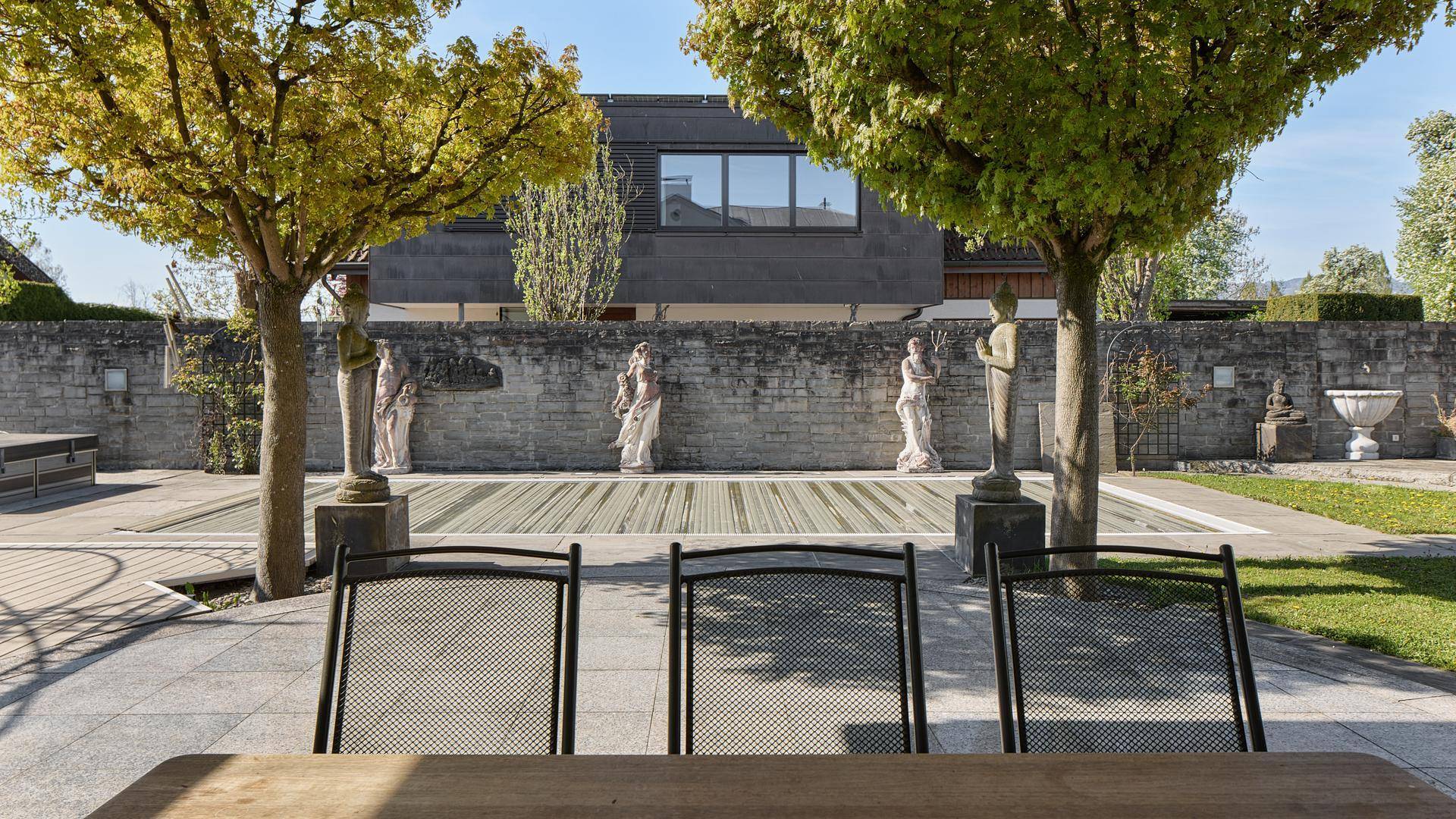 Mediterraner Gartenbereich mit Statuen, Poolabdeckung und Sitzgelegenheiten.