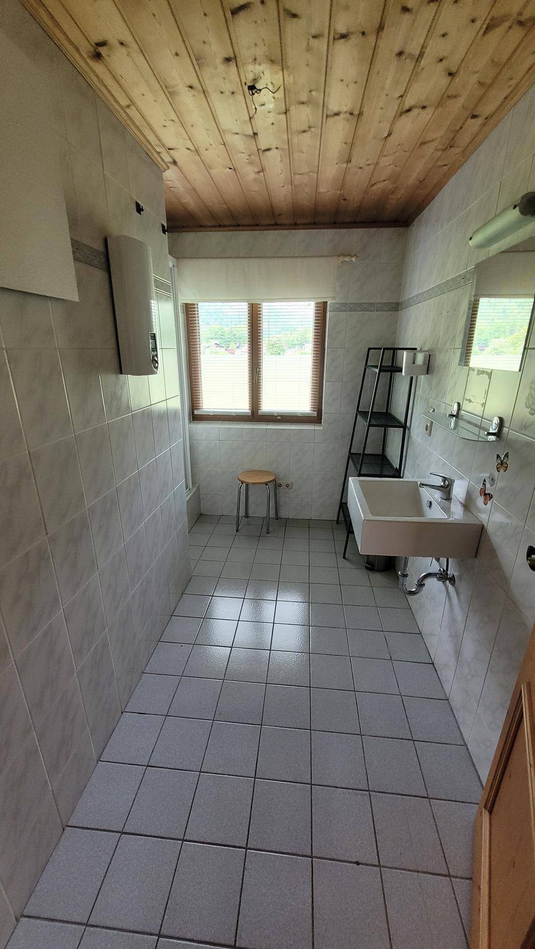 Schlichtes Badezimmer mit Fliesenboden, Waschbecken und Fenster für natürliche Belüftung.