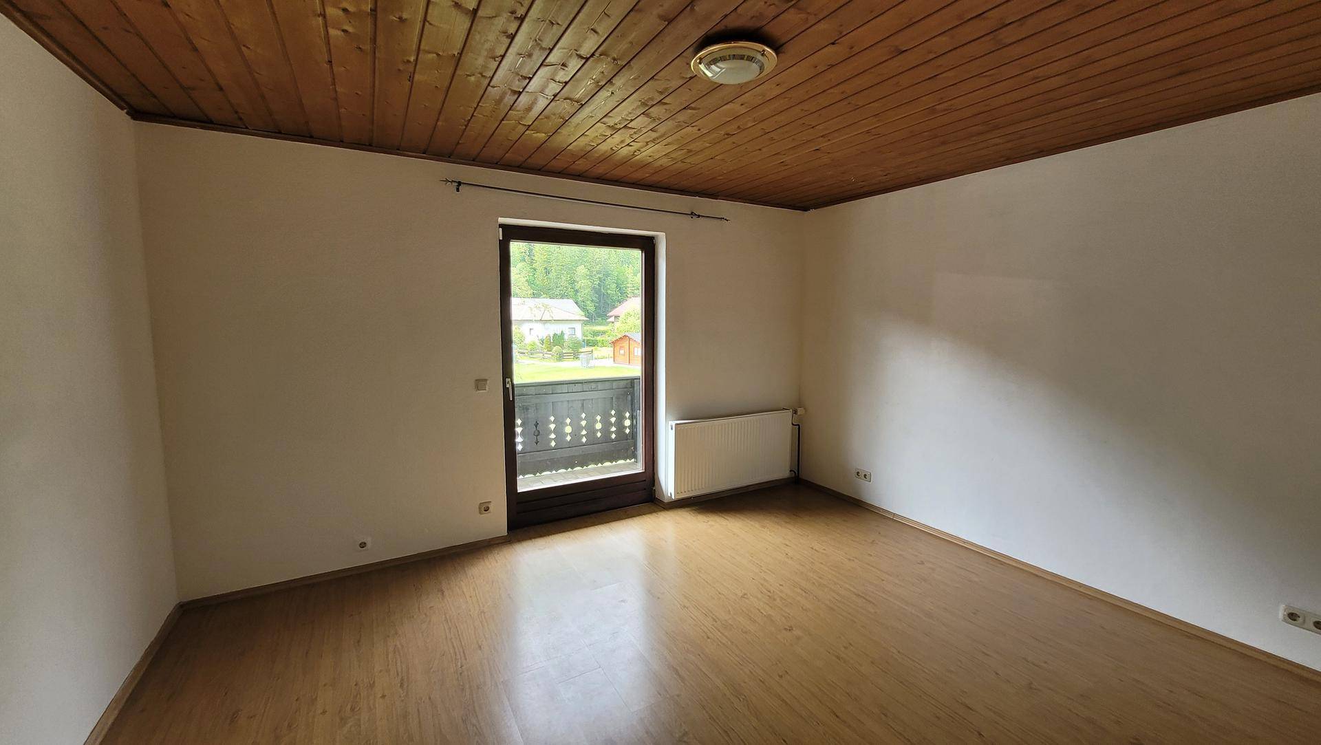Leeres Schlafzimmer mit Holzboden, Heizkörper und Zugang zu einem kleinen Balkon.