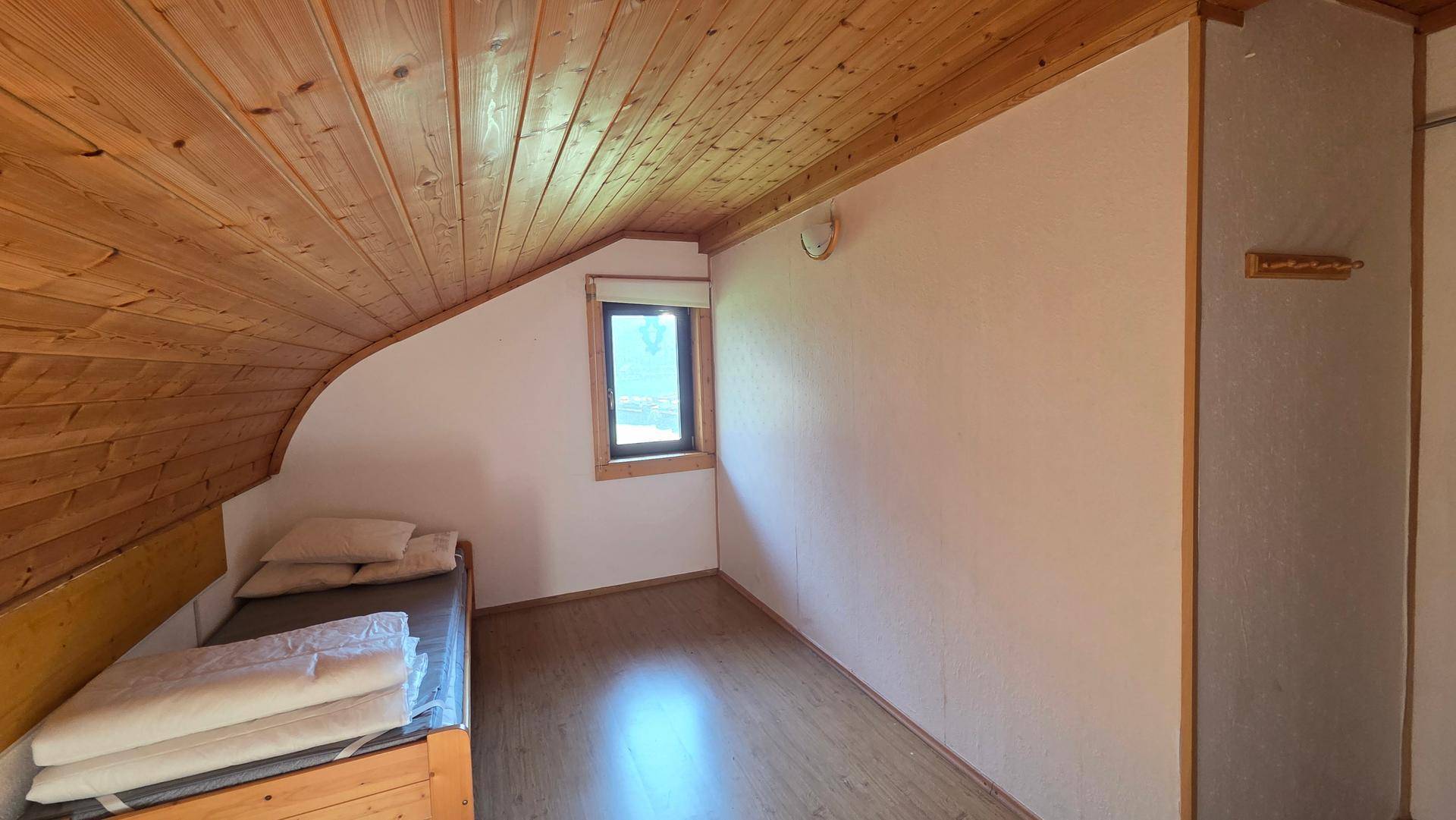 Gemütliches Schlafzimmer mit Holzboden, Dachschrägen und einem kleinen Fenster.