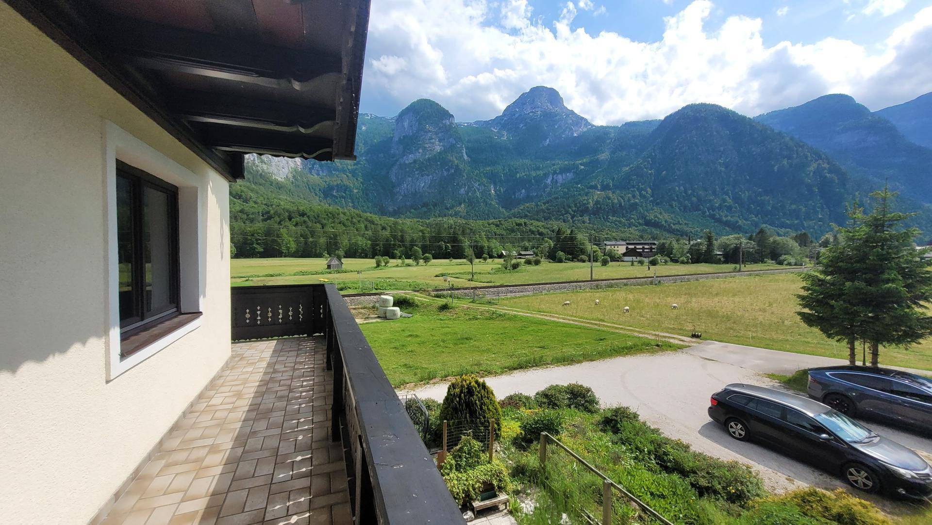 Großer Balkon mit Fliesenboden und einem weiten Panoramablick auf die Berge und grüne Landschaft.
