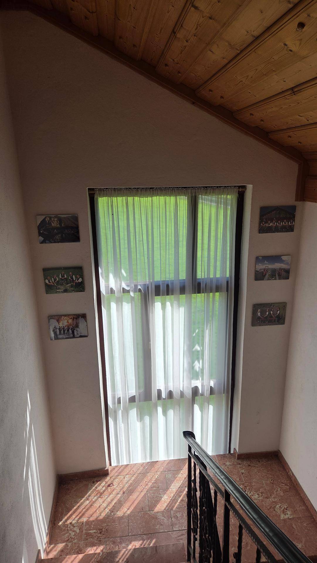 Helles Treppenhaus mit Holzdecke, Marmorstufen und einem großen Fenster mit transparenten Vorhängen.