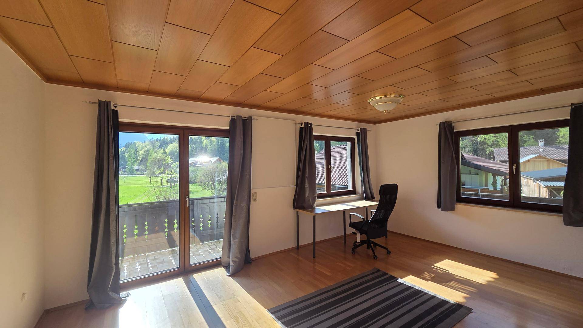 Helles Arbeitszimmer mit Holzbalkendecke, Holzboden und Zugang zu einem Balkon mit Bergblick.