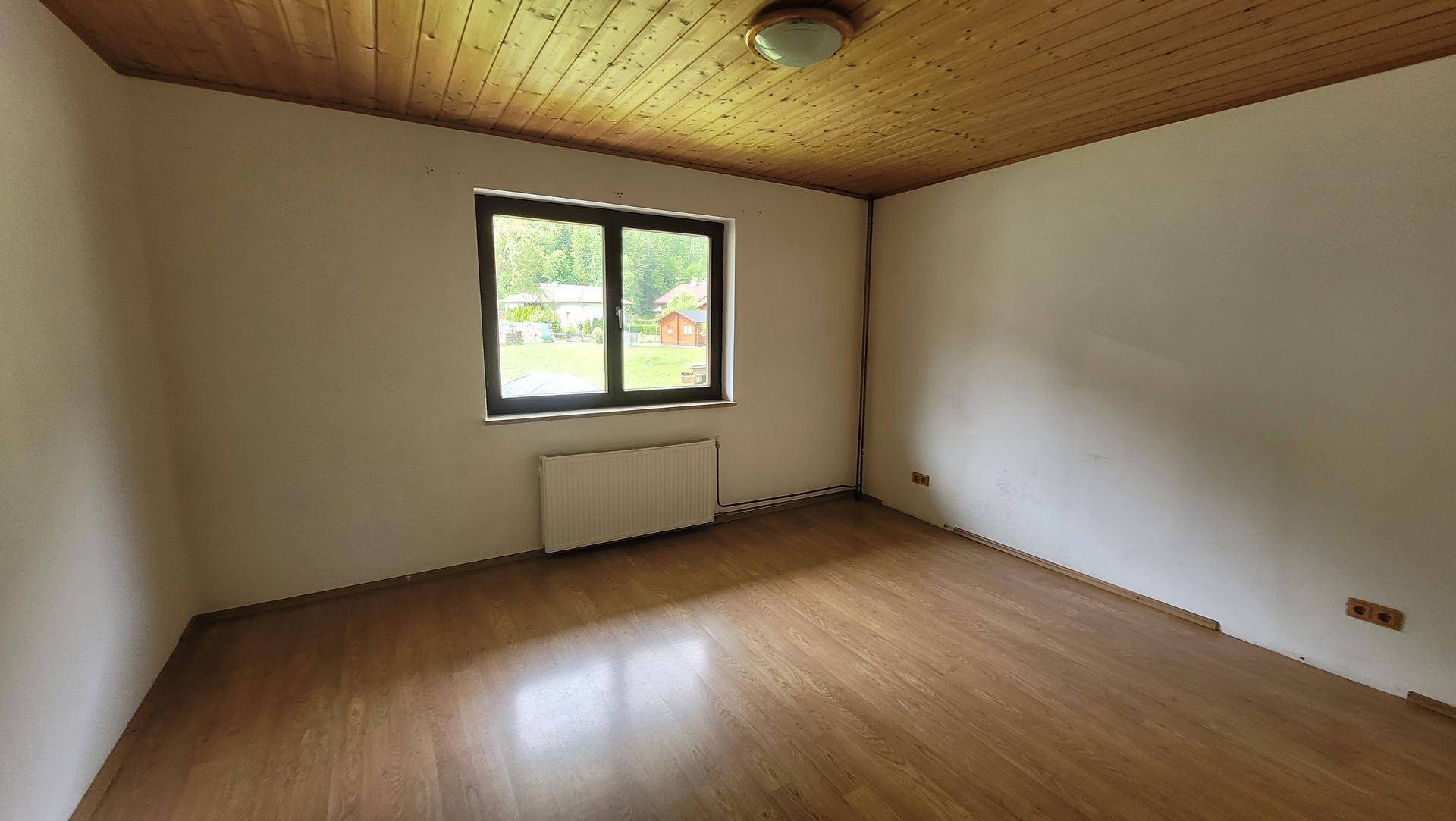Helles Schlafzimmer mit Holzbalkendecke, Holzboden und Fenster mit einem beruhigenden Blick ins Grüne.