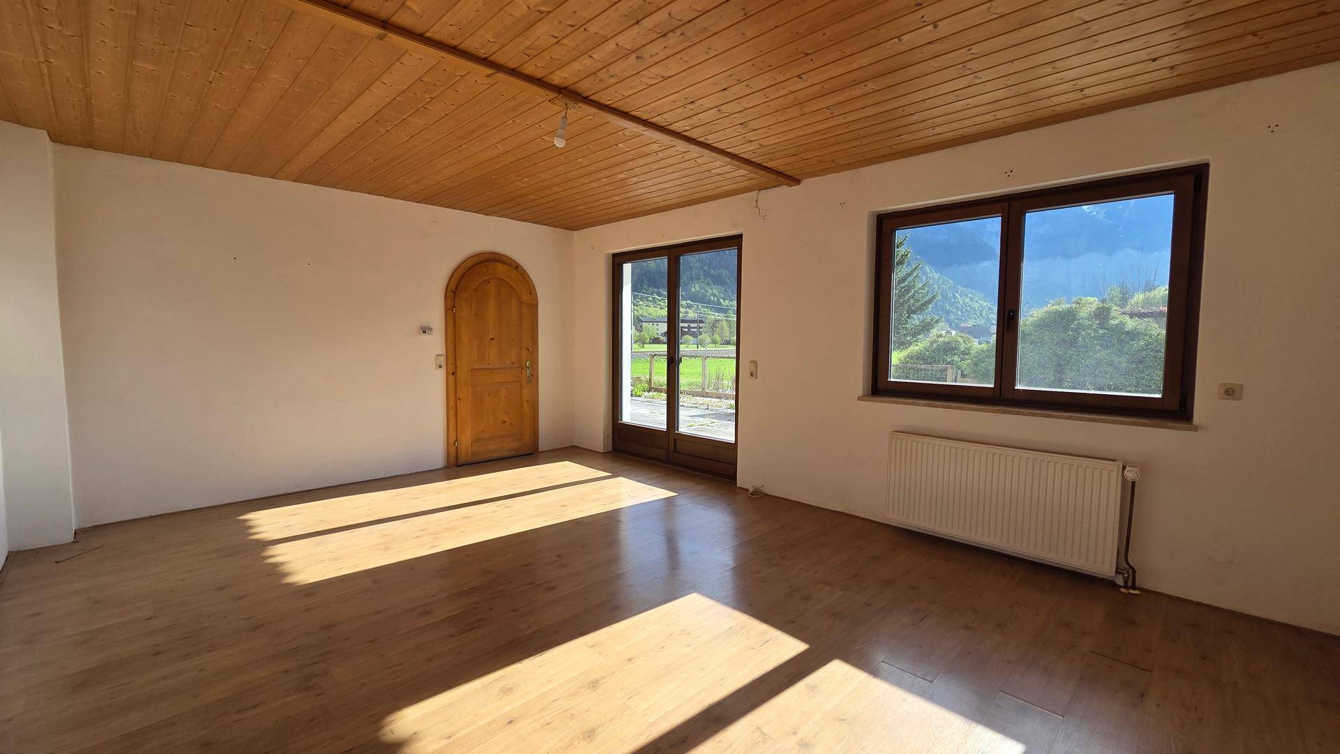 Heller Wohnraum mit Holzbalkendecke, Holzboden und Zugang zu einem Außenbereich mit Bergblick.