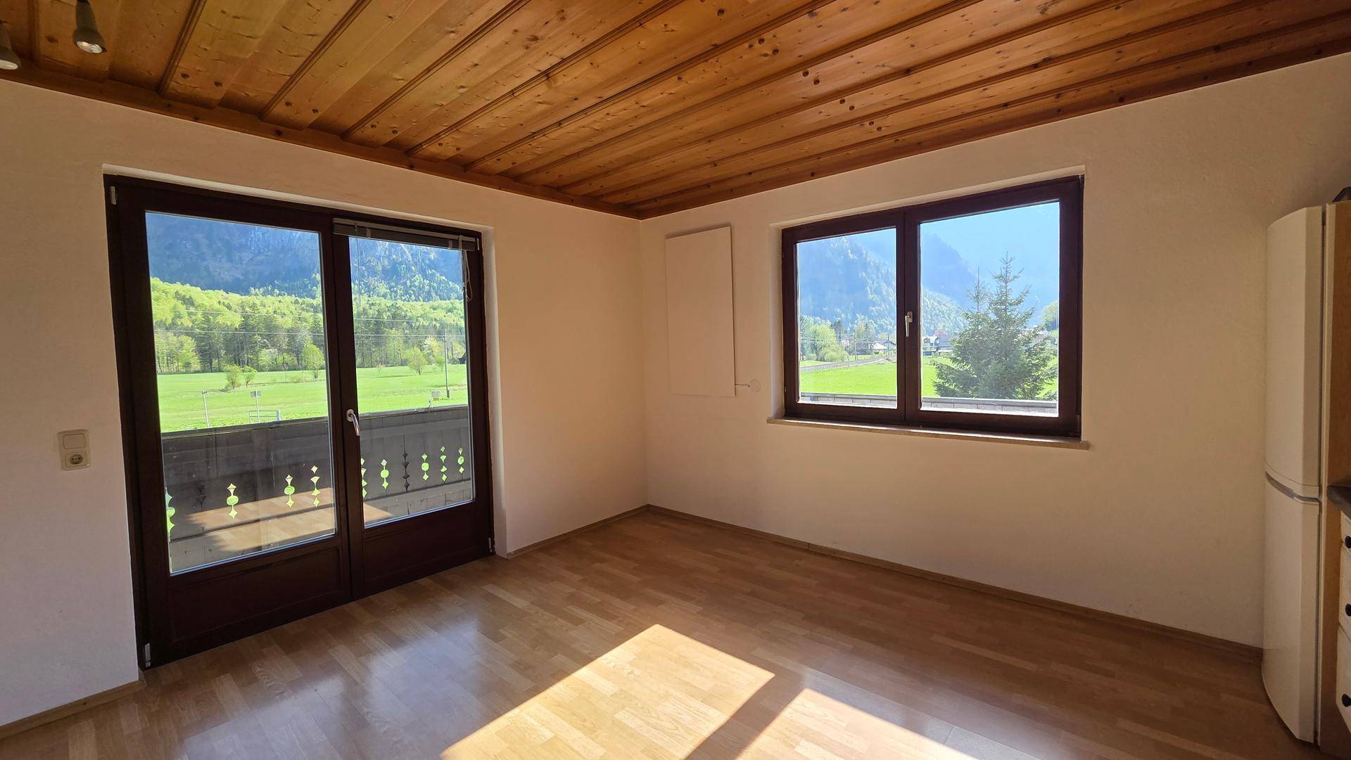 Heller Wohnraum mit Holzbalkendecke, Holzboden und Zugang zu einem Balkon mit Bergblick.