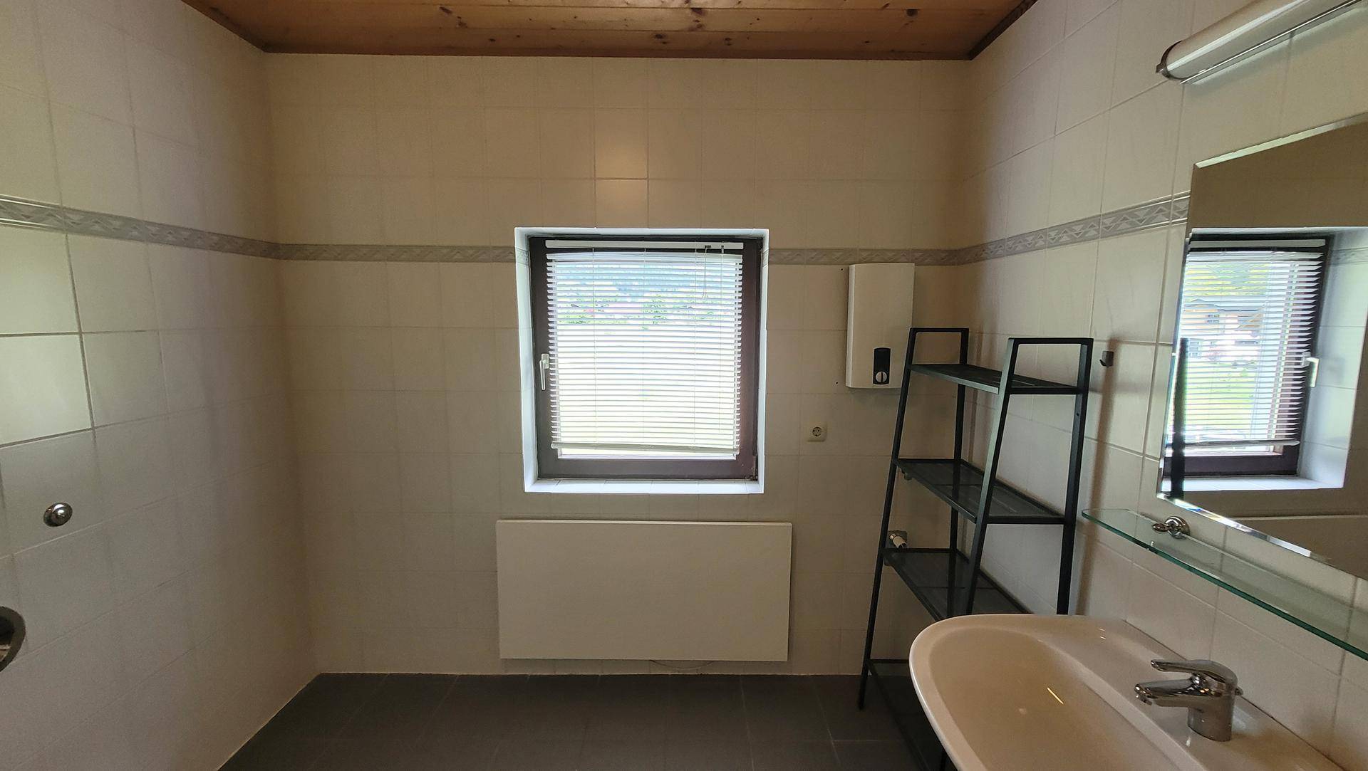 Helles Badezimmer mit Waschbecken, Spiegel und Fenster, das viel Tageslicht hereinlässt.