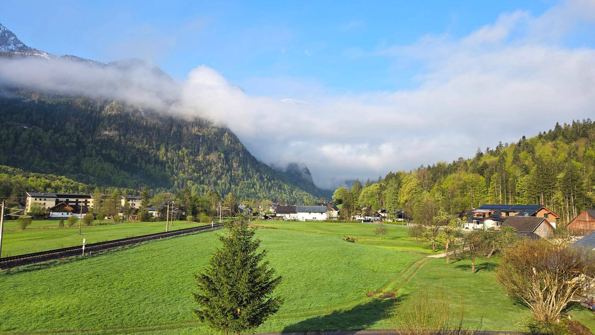 Panoramablick auf die grüne Landschaft mit Häusern und nebelverhangenen Bergen am Morgen.