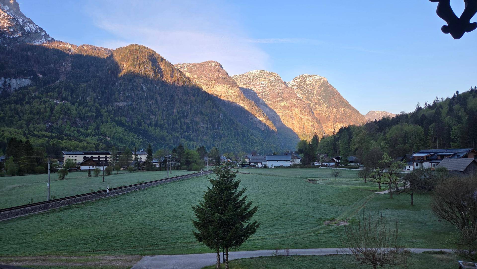 Malerischer Morgenblick auf die sonnenbeschienenen Berge und grüne Wiesen mit Häusern im Tal.