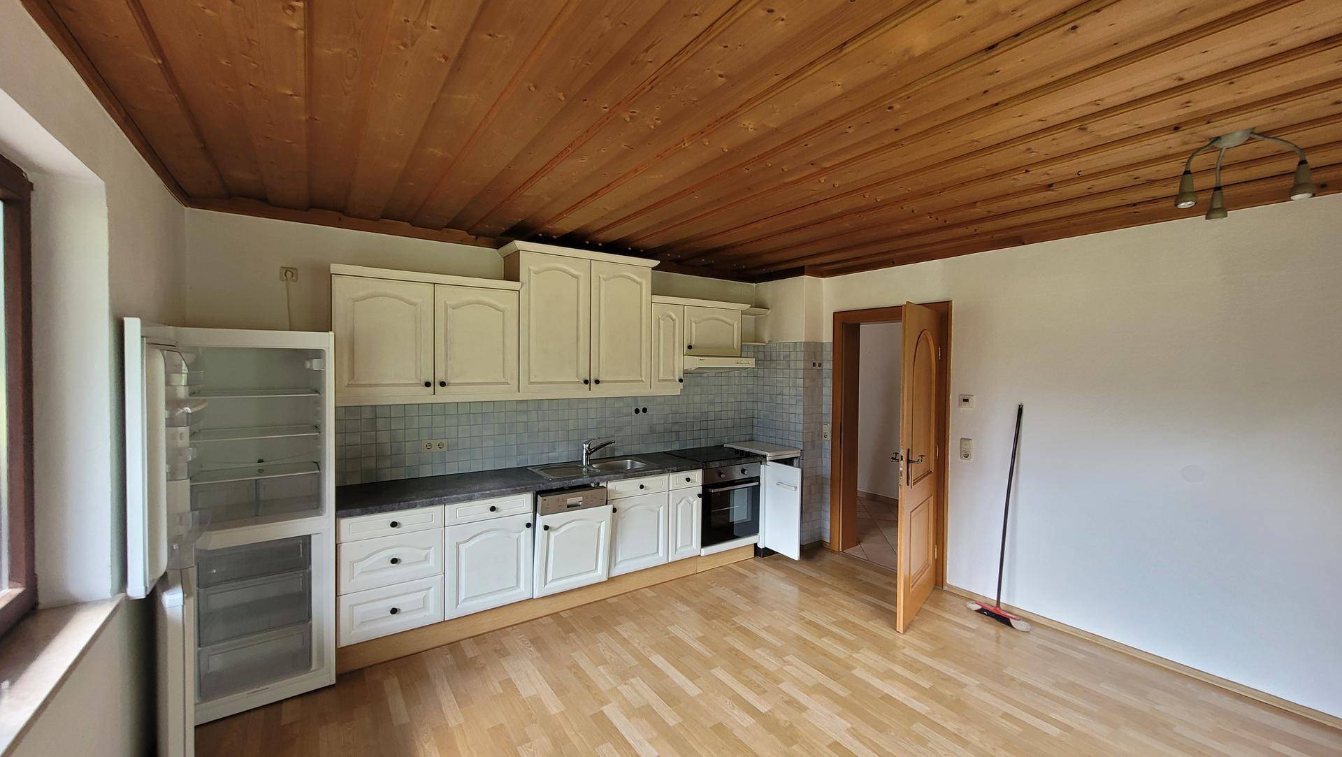 Geräumige Küche mit weißen Schränken, Holzbalkendecke und viel Tageslicht, inklusive Geräten.