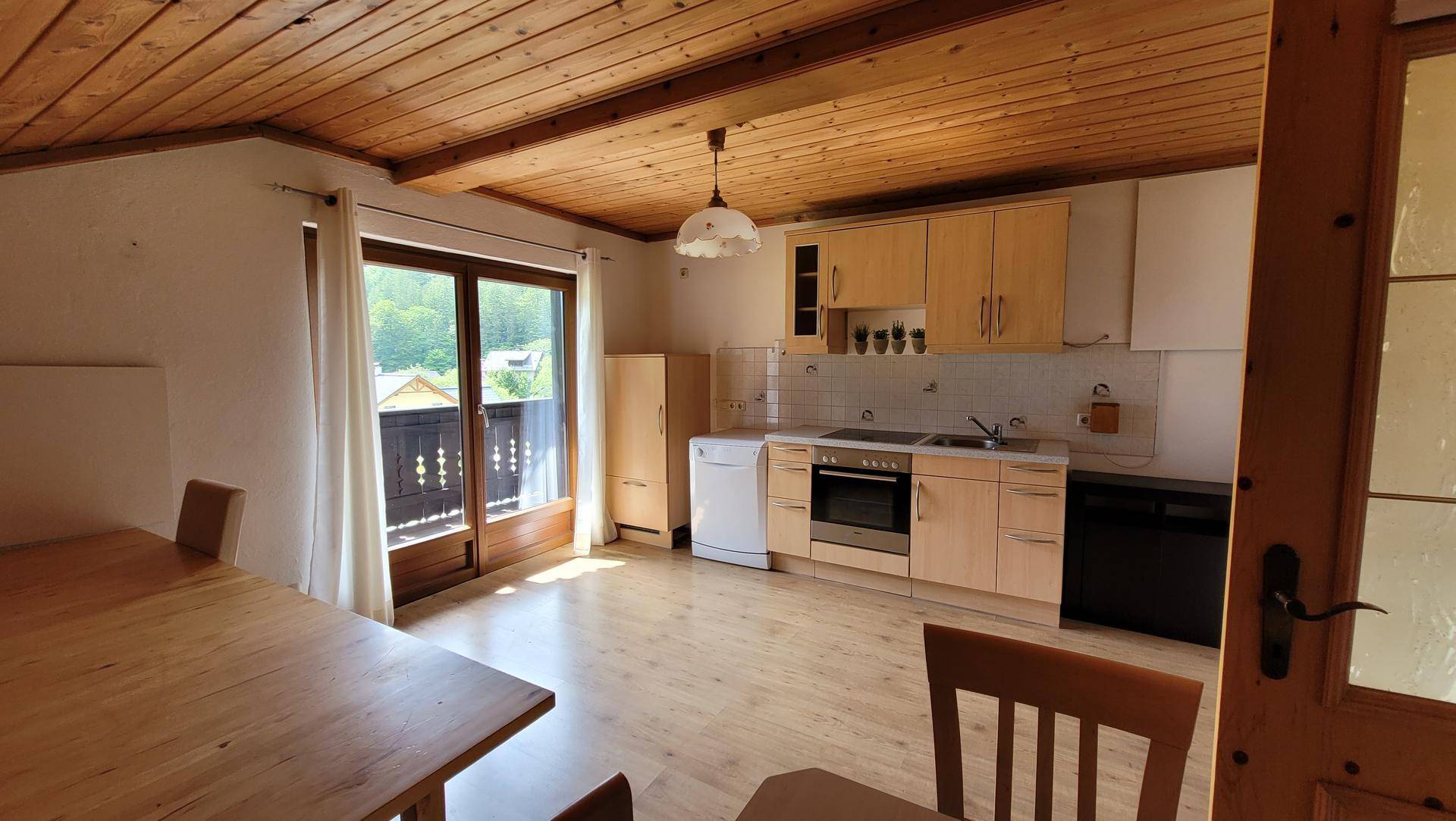 Helle Wohnküche mit Holzeinbauten, Esstisch und Zugang zu einem Balkon mit Bergblick.