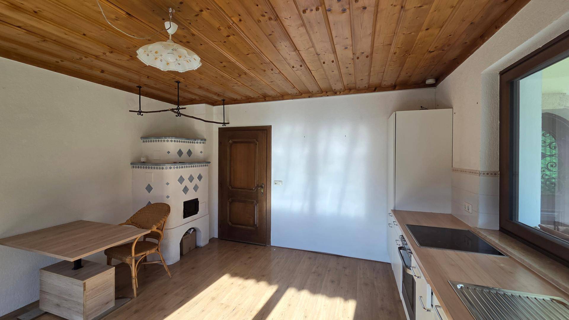 Gemütliche Küche mit traditionellem Kachelofen, Holzbalkendecke und einem praktischen Essbereich.