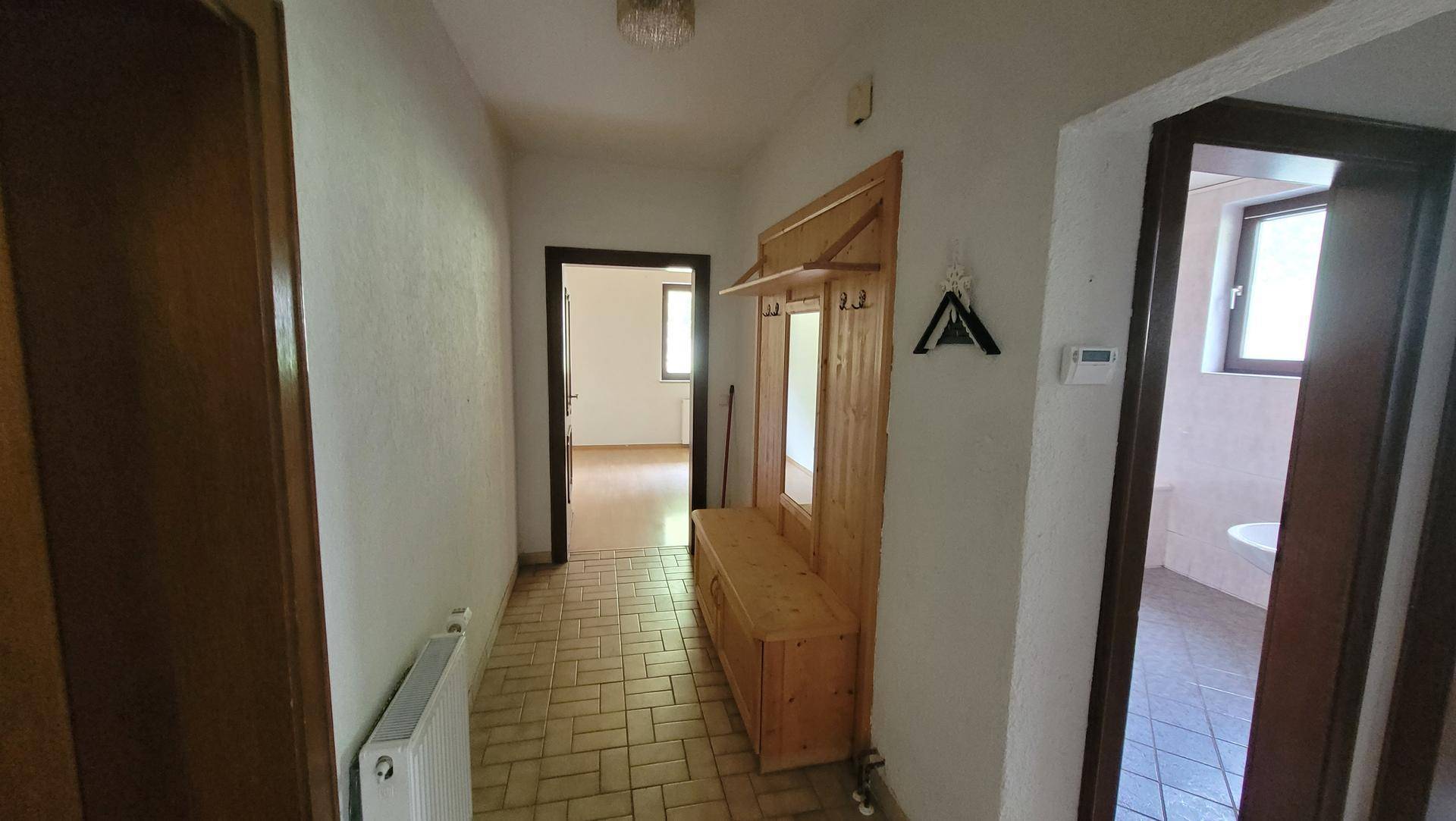 Heller Flur mit traditioneller Holzgarderobe, Fliesenboden und Blick in angrenzende Räume.
