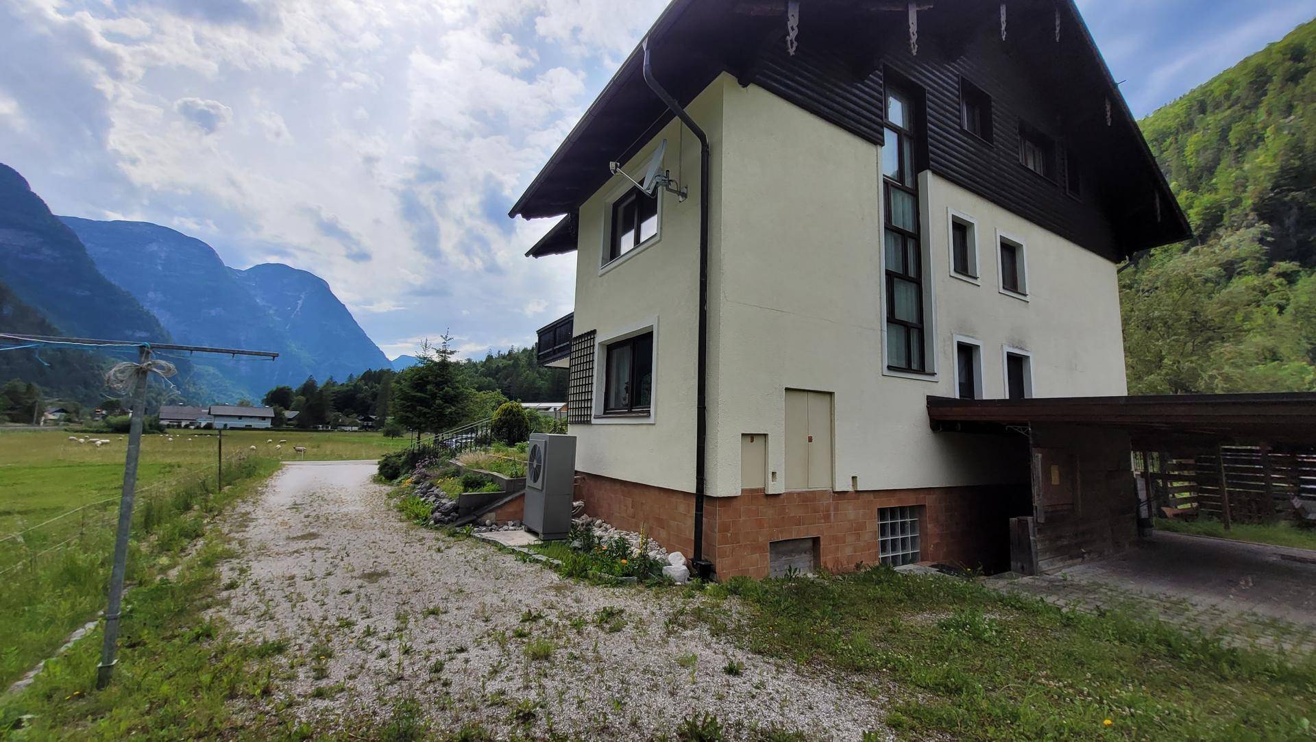 Seitenansicht eines Hauses mit Carport, umgeben von Bergen und grüner Landschaft.