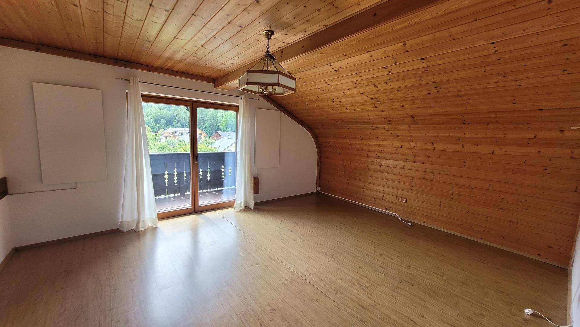 Geräumiges Zimmer mit Holzboden, Dachschrägen und Zugang zu einem Balkon mit Aussicht.