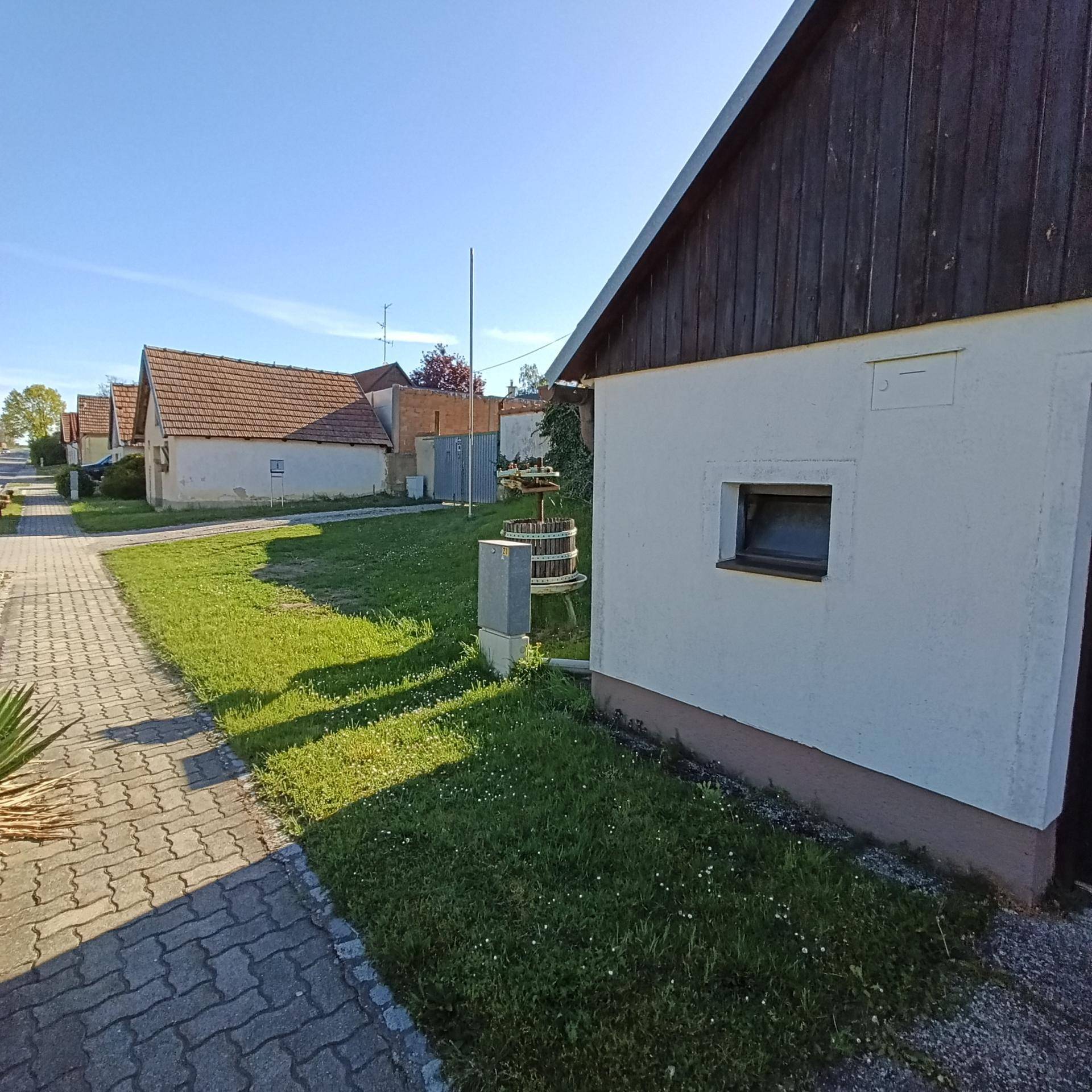Seitenansicht des Gebäudes mit einem gepflasterten Weg und weiteren Häusern in der Ferne unter blauem Himmel.