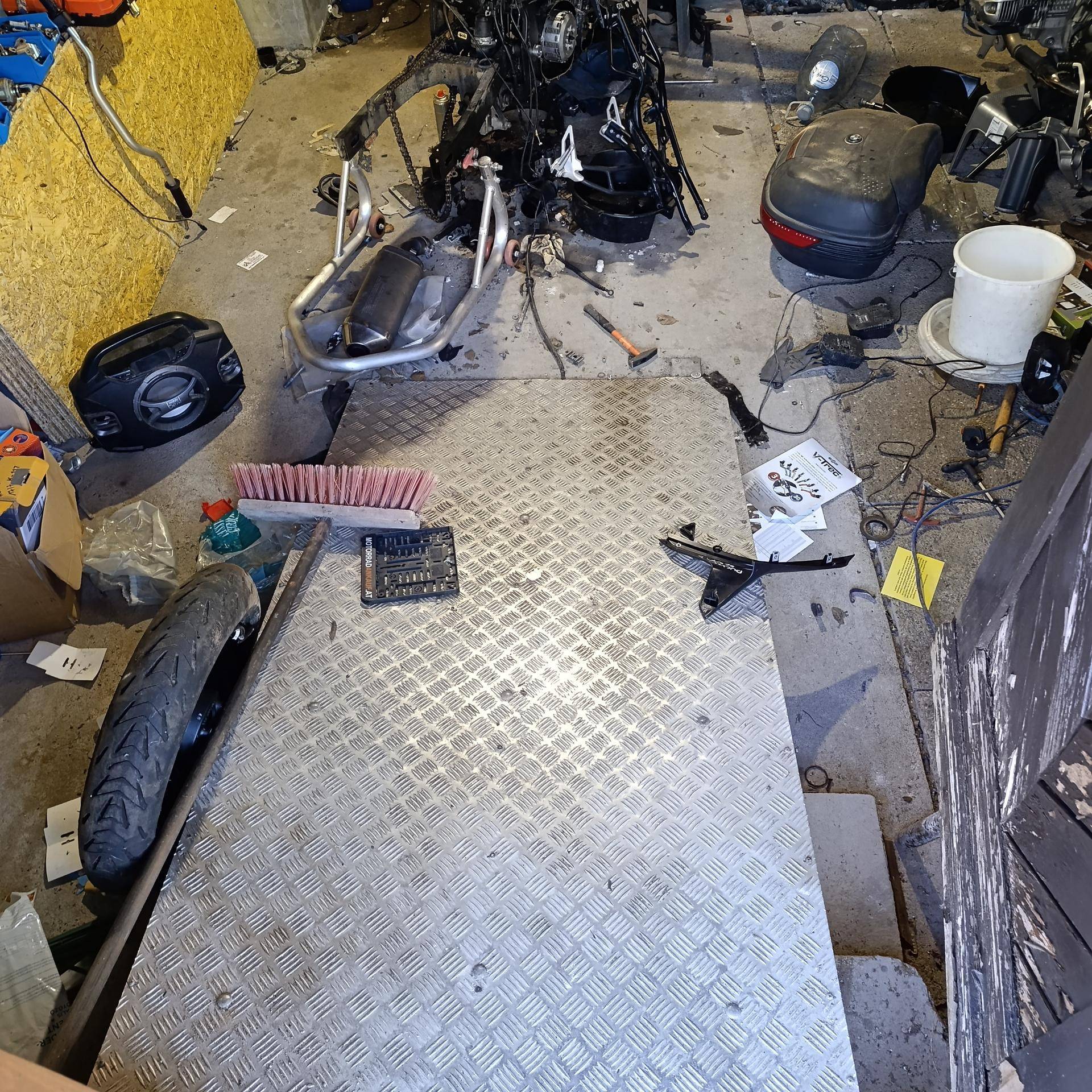 Ein unordentlicher Werkstattbereich mit einem Motorradrahmen, Werkzeugen und einer Metallplatte auf dem Boden.